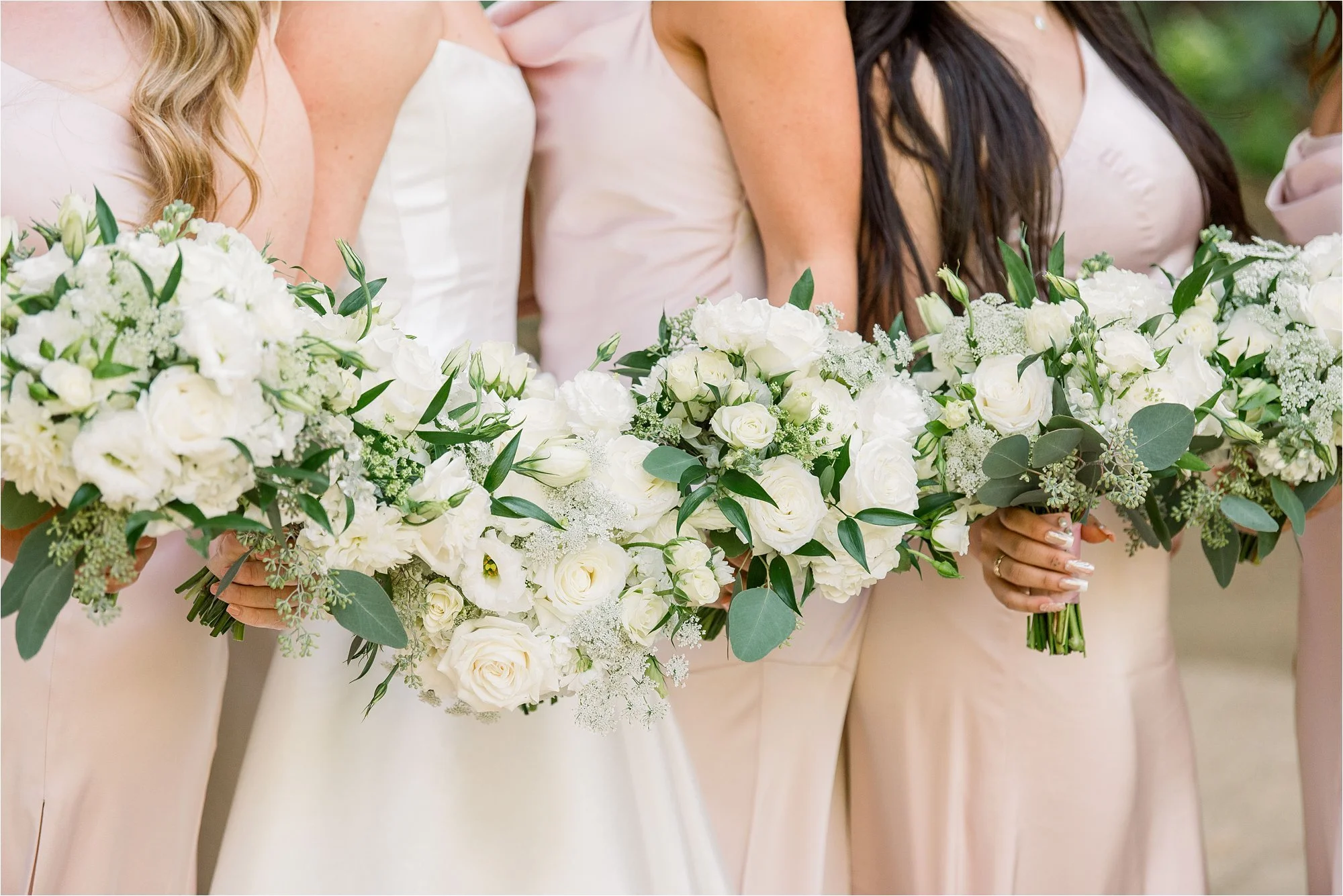 Closeup of white floral bouquets with Bride and Bridesmaids wearing soft pink satin dresses