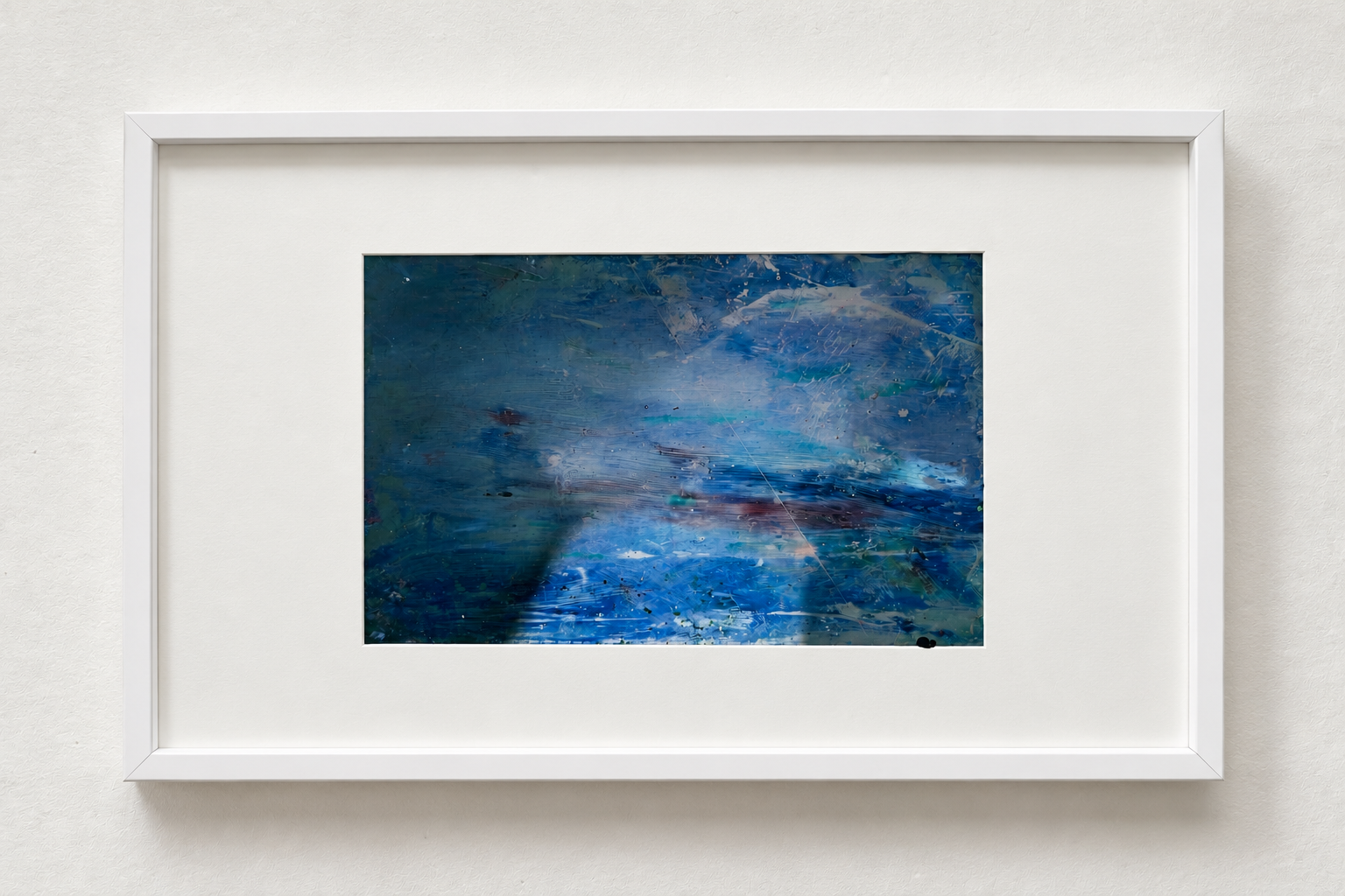 Abstract painting with blue, green, and white colors framed in white hanging on a white wall.