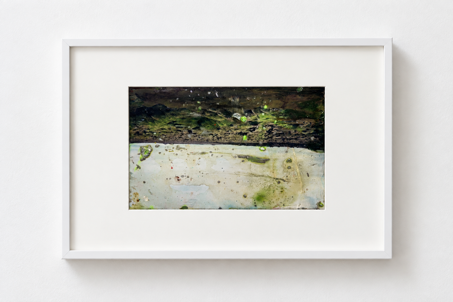 A framed abstract painting with dark green, black, and beige colors, featuring textured layers and scattered spots, mounted on a white wall.