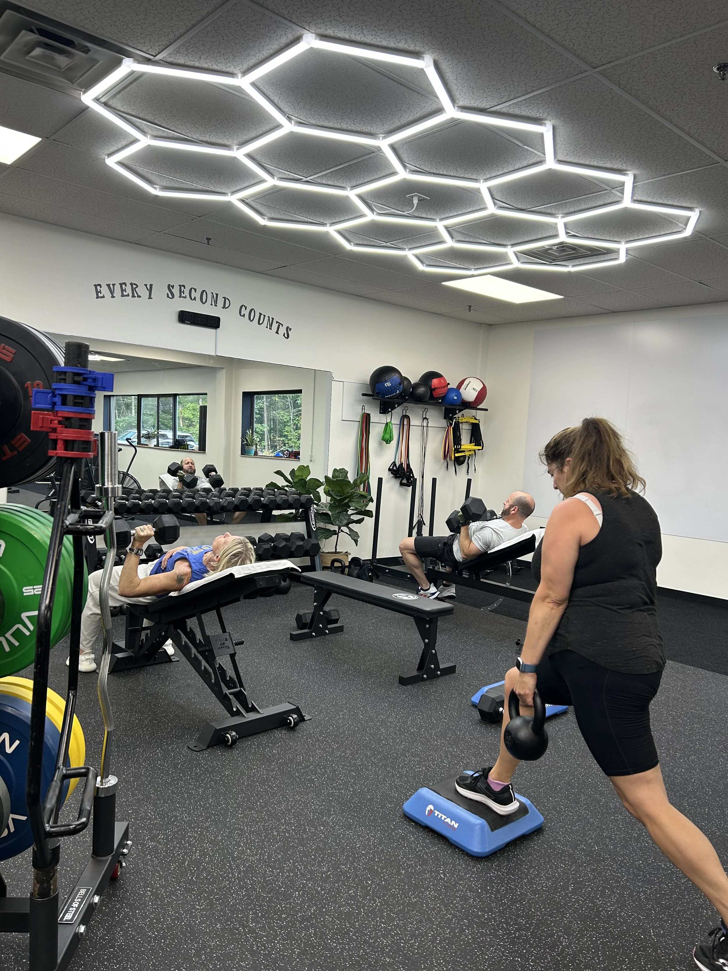 Two women exercising in a gym, lifting kettlebells and using a workout bench.