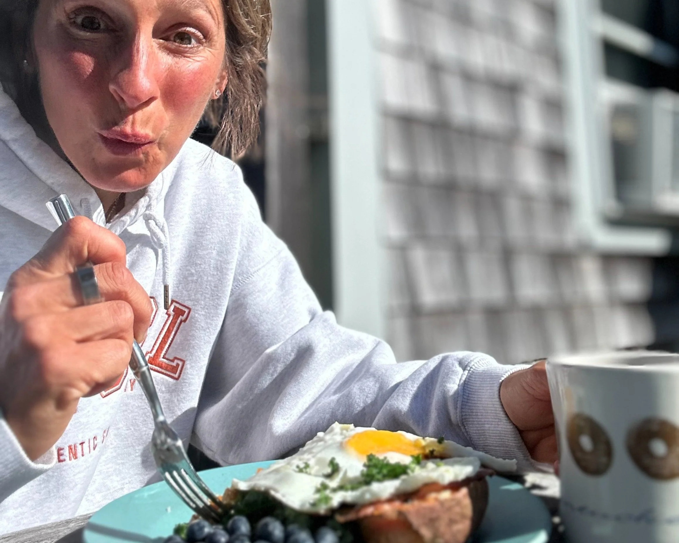 Two women exercising with kettlebells in a gym, one bending forward lifting a kettlebell, and other standing with a kettlebell, with gym equipment and lockers in the background.