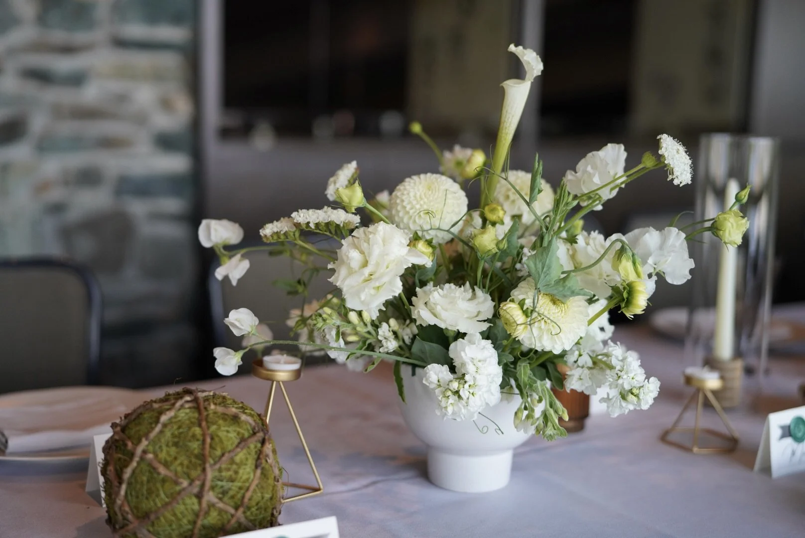 White floral centerpiece on a table with candles and decorative items, set in a rustic indoor setting.
