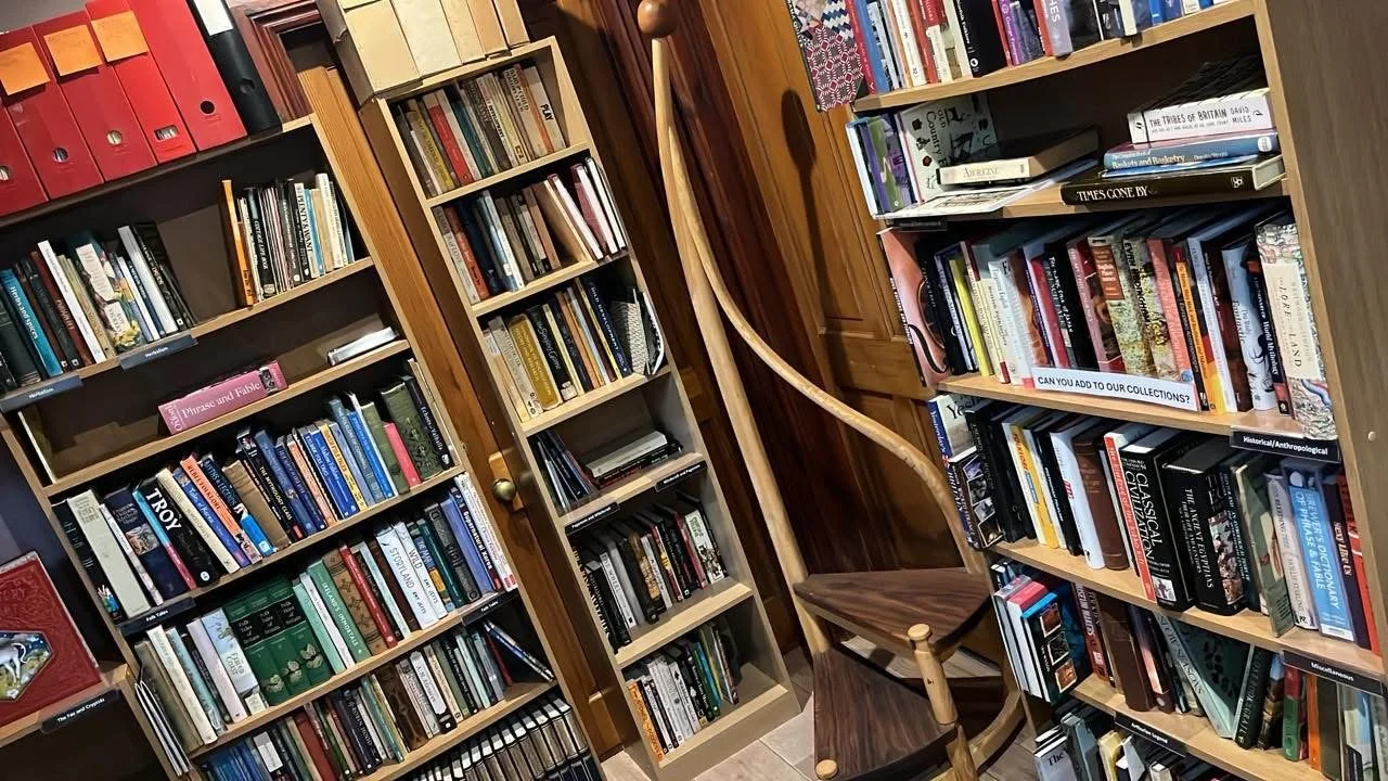 A small room with bookshelves filled with books, a wooden chair, and a coat rack.