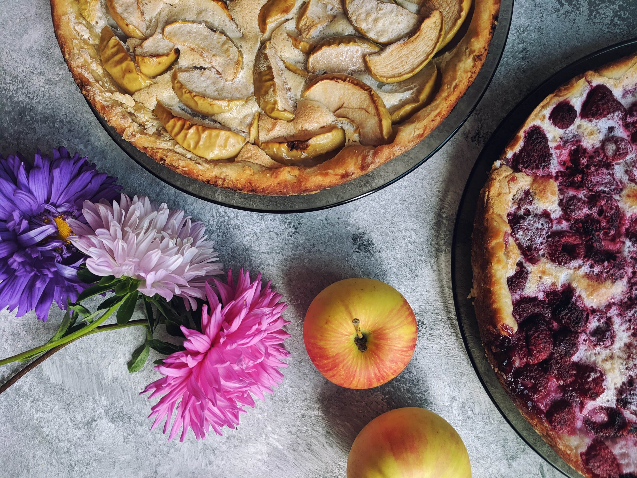 purple and pink flowers beside two freshly baked pies, apple and raspberry