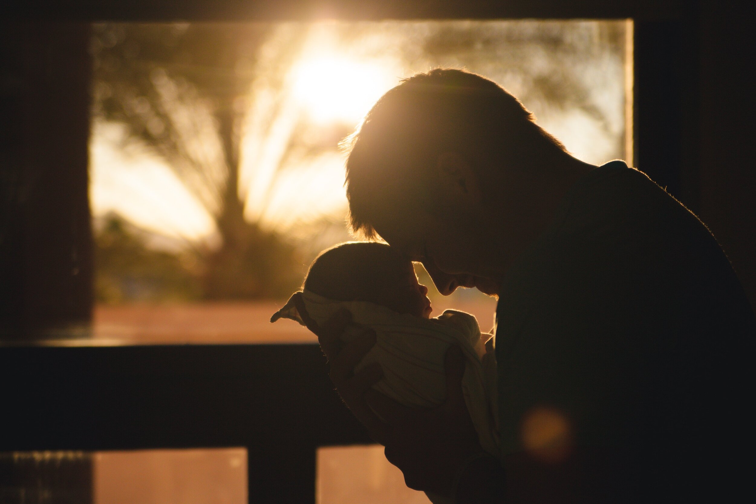 father touches forehead to his newborn baby's forehead during sunset