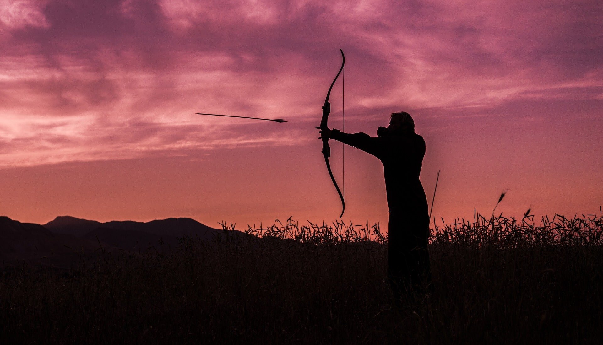 woman fires bow and arrow at sunset