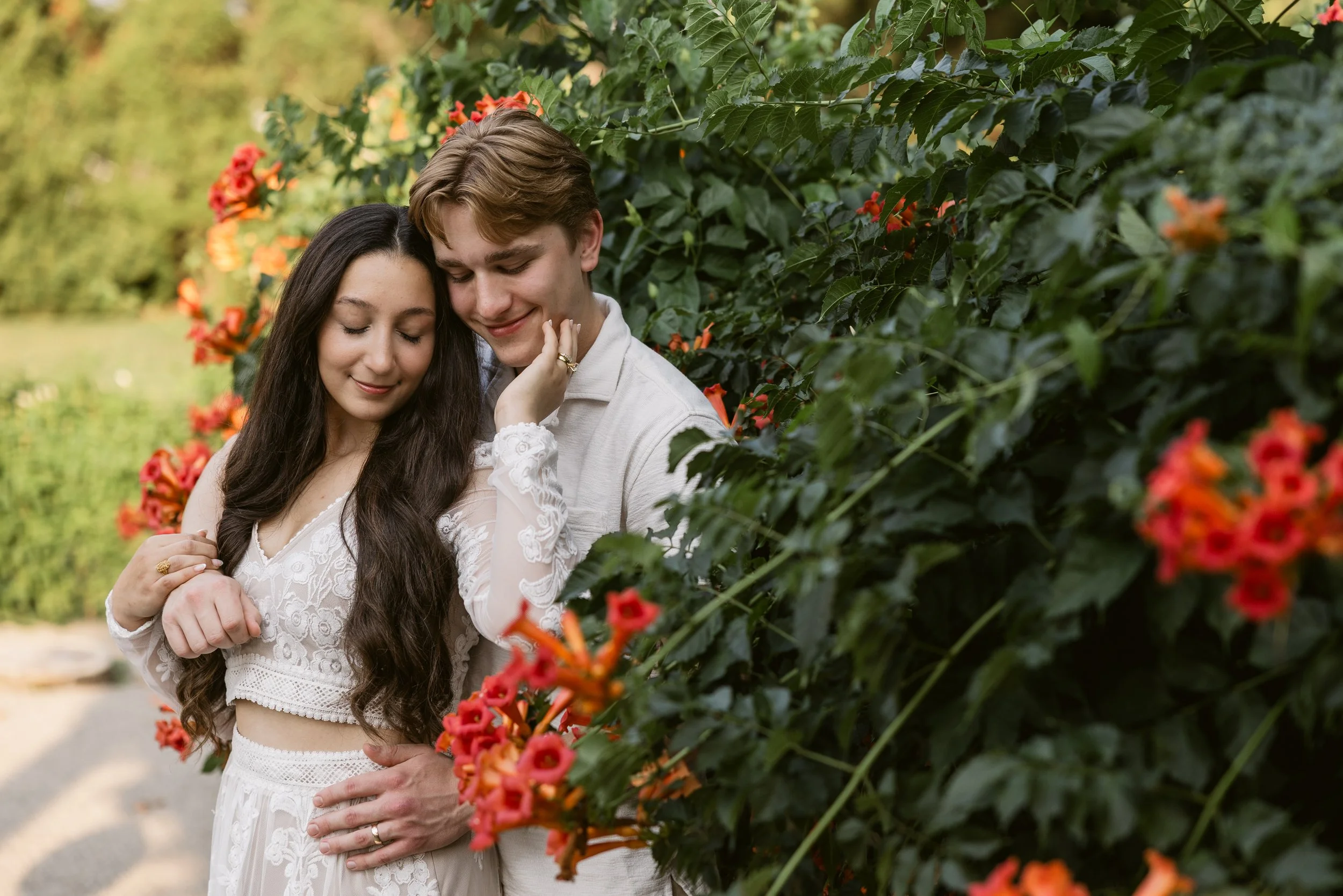 Engaged couple embracing among orange flowering shrubs in Macomb County