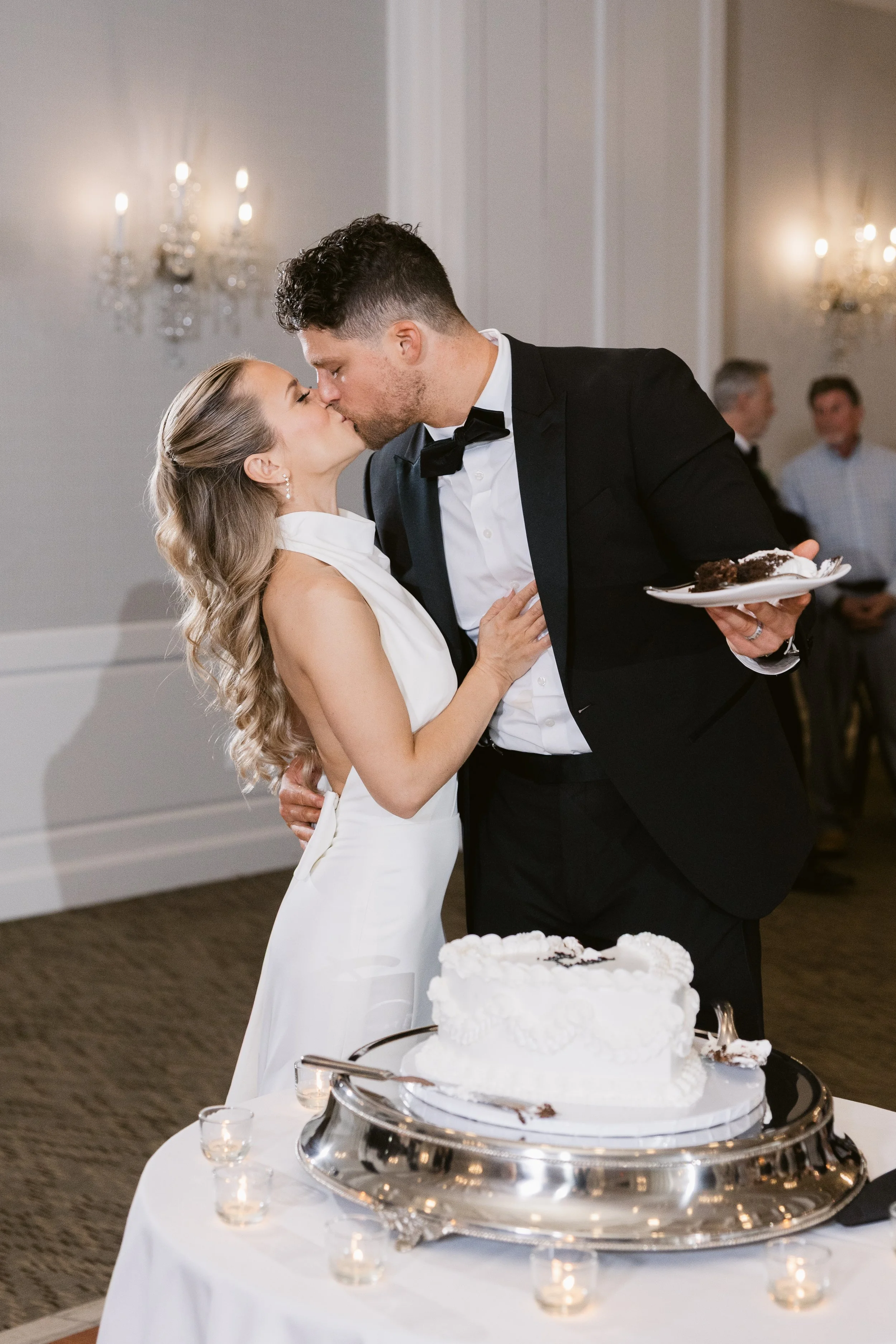 Bride and groom kissing beside their wedding cake at an elegant Michigan reception