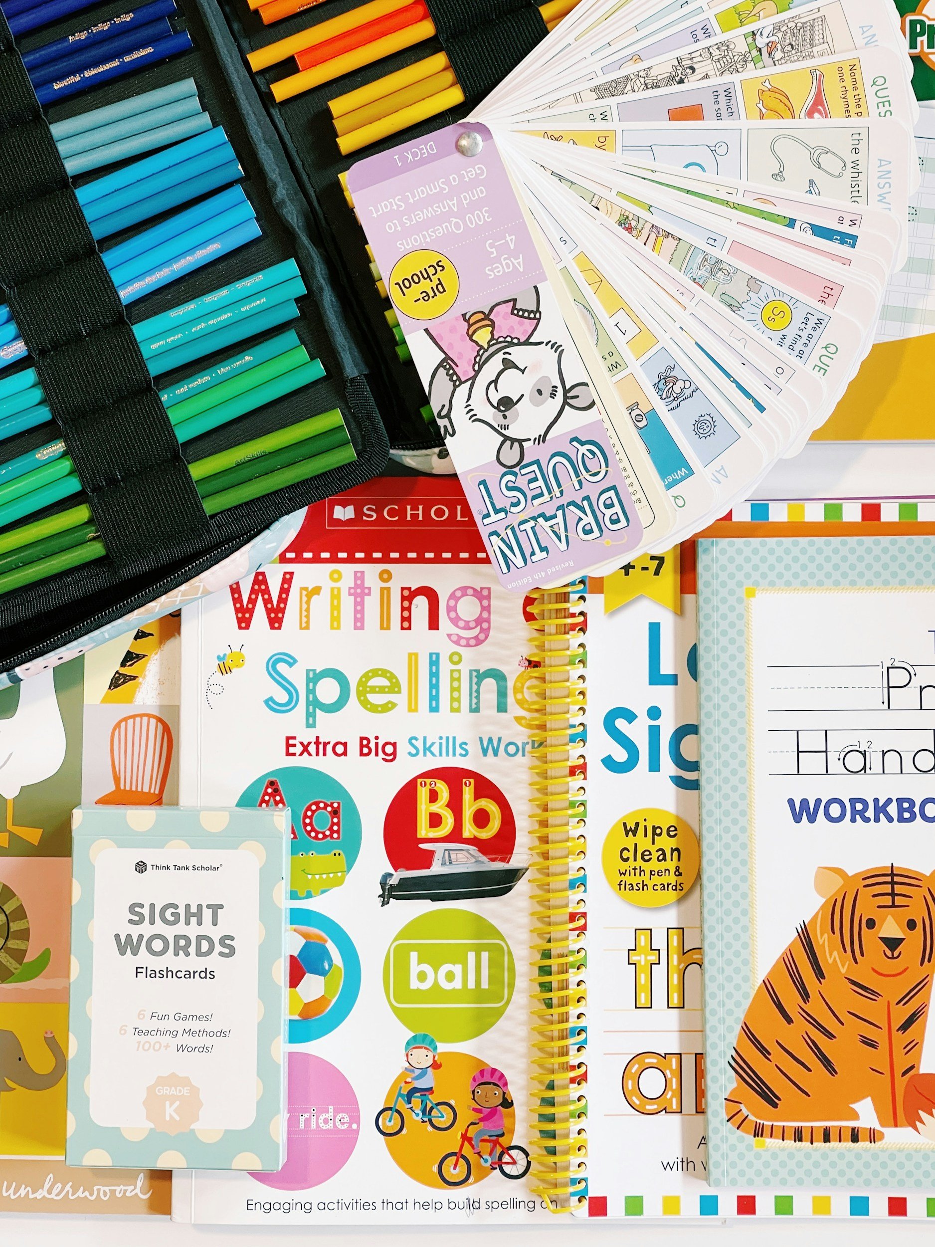 Shot of educational materials for young children, including sight word flashcards, spelling and writing books, and a learning kit with colored markers.