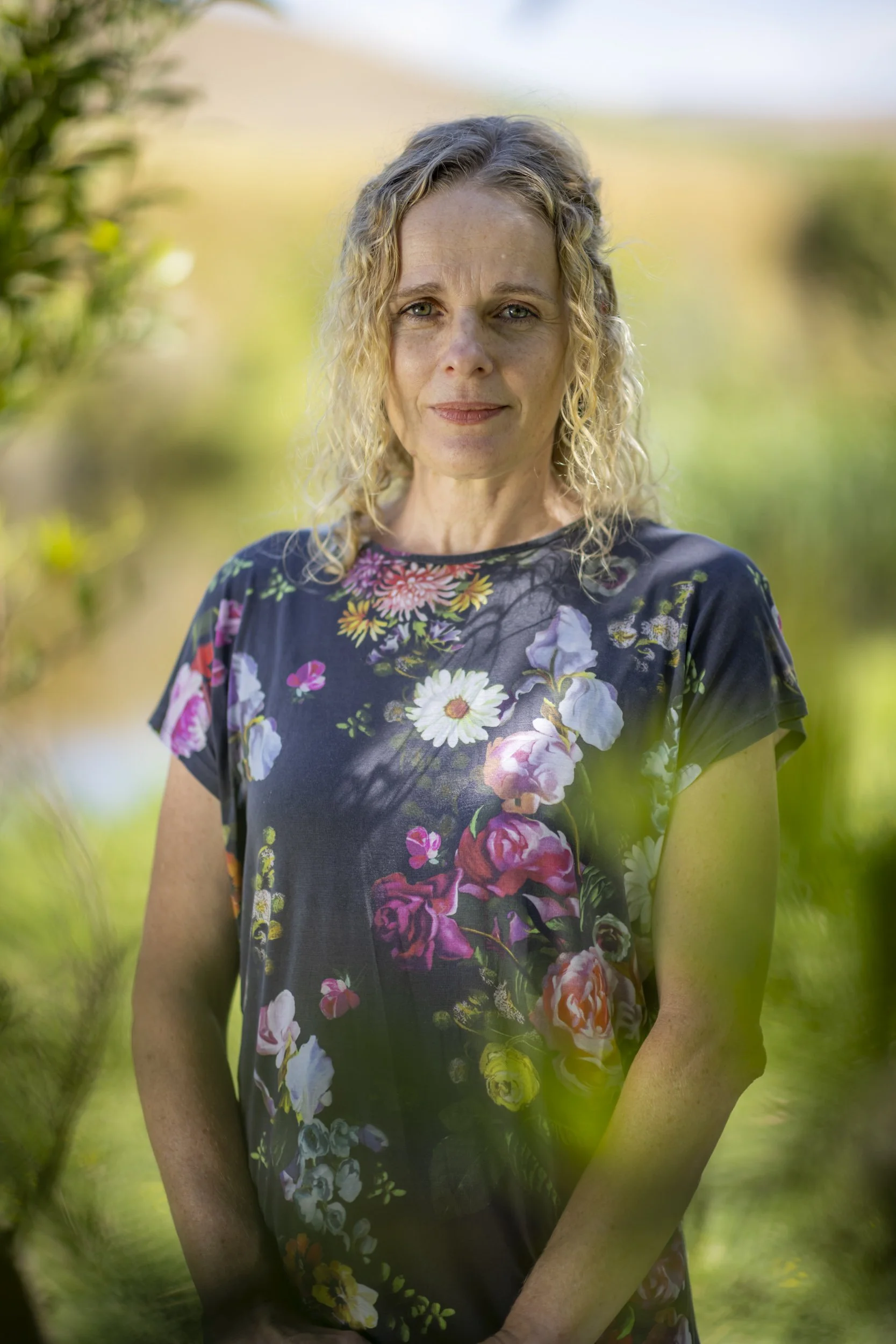 Woman in a floral shirt with blond curly hair smiling.