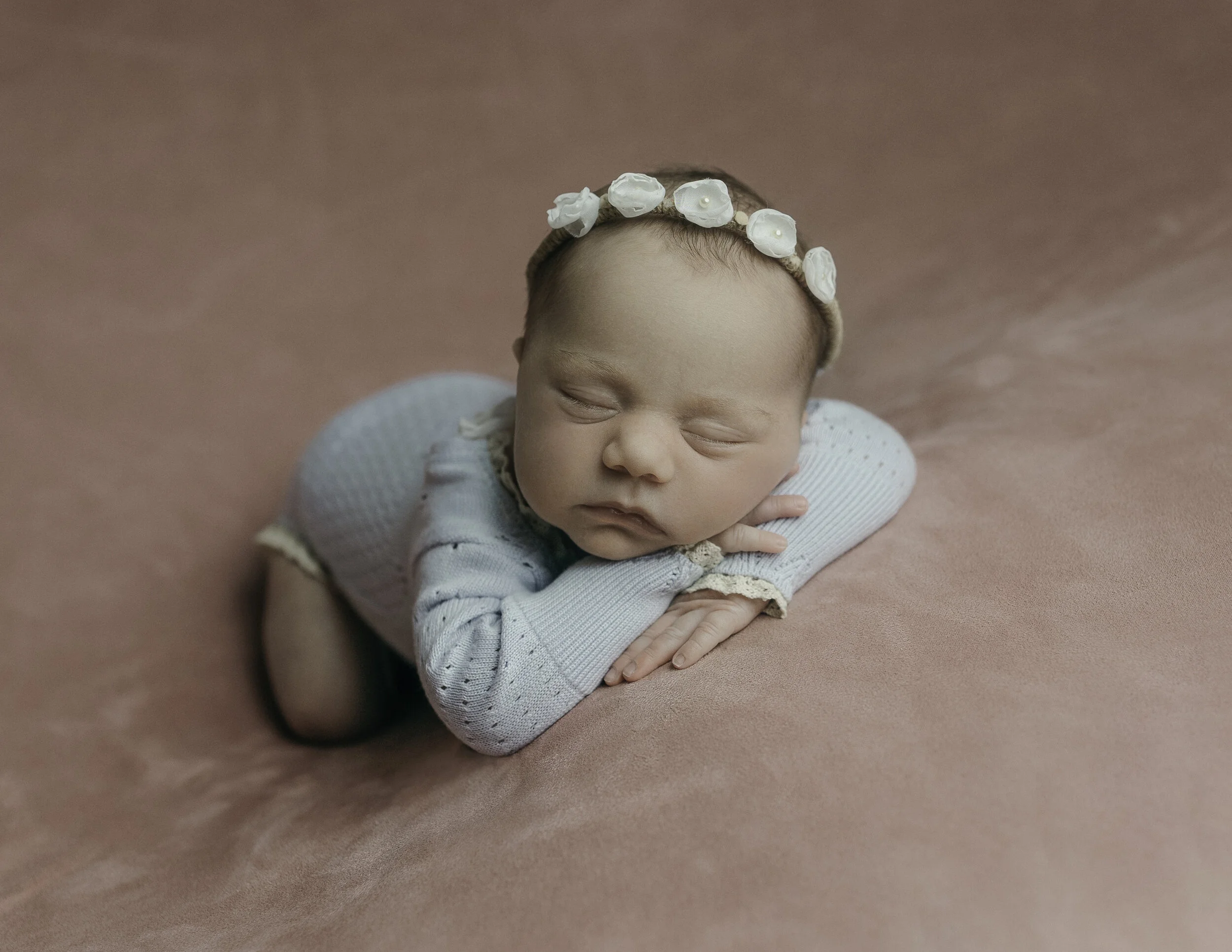 baby girl posed with chin on hands wearing a blue outfit in a pink backdrops