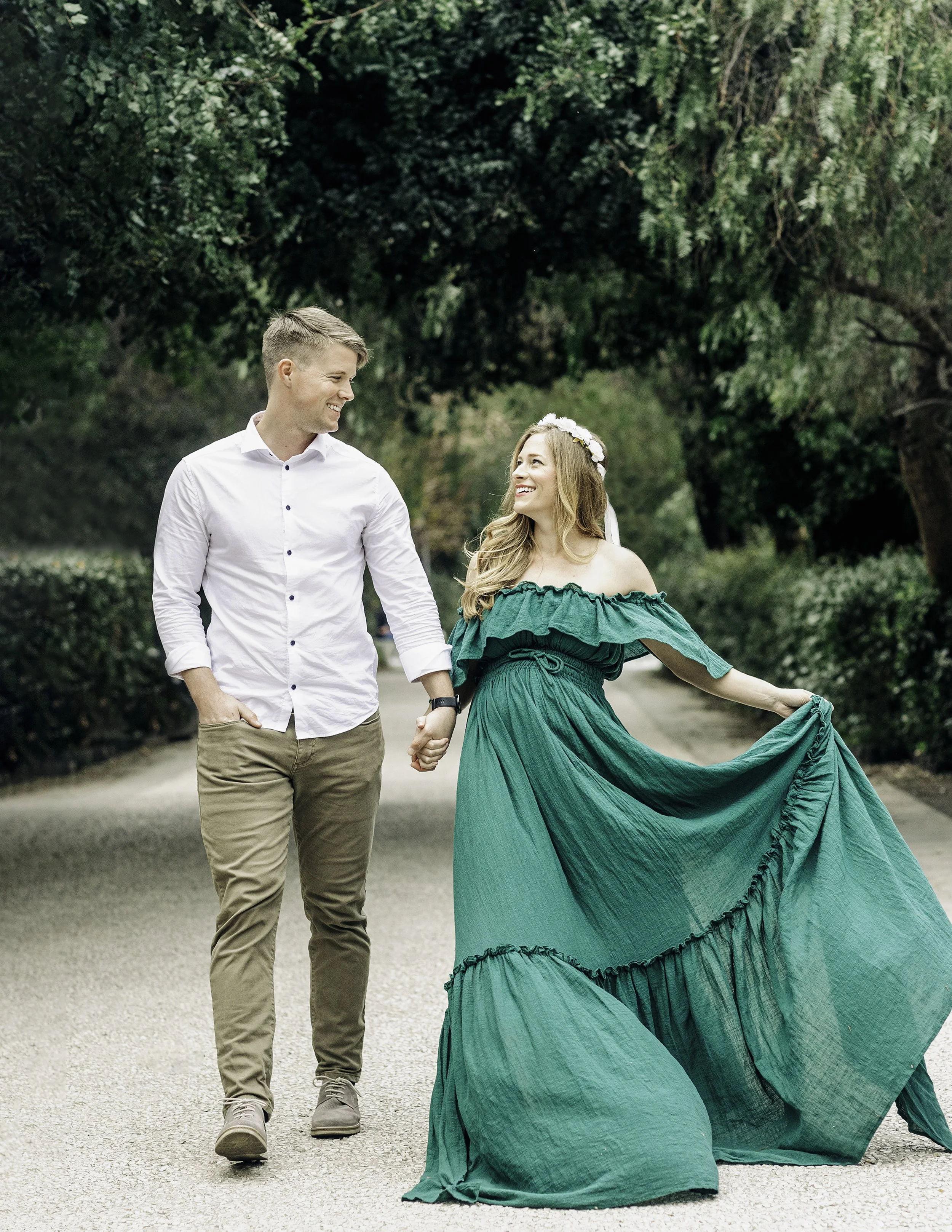 Maternity portrait of a couple holding hands and walking while looking and smiling at each other tane in a greenery tunnel at the Bellini Gardens in Catania