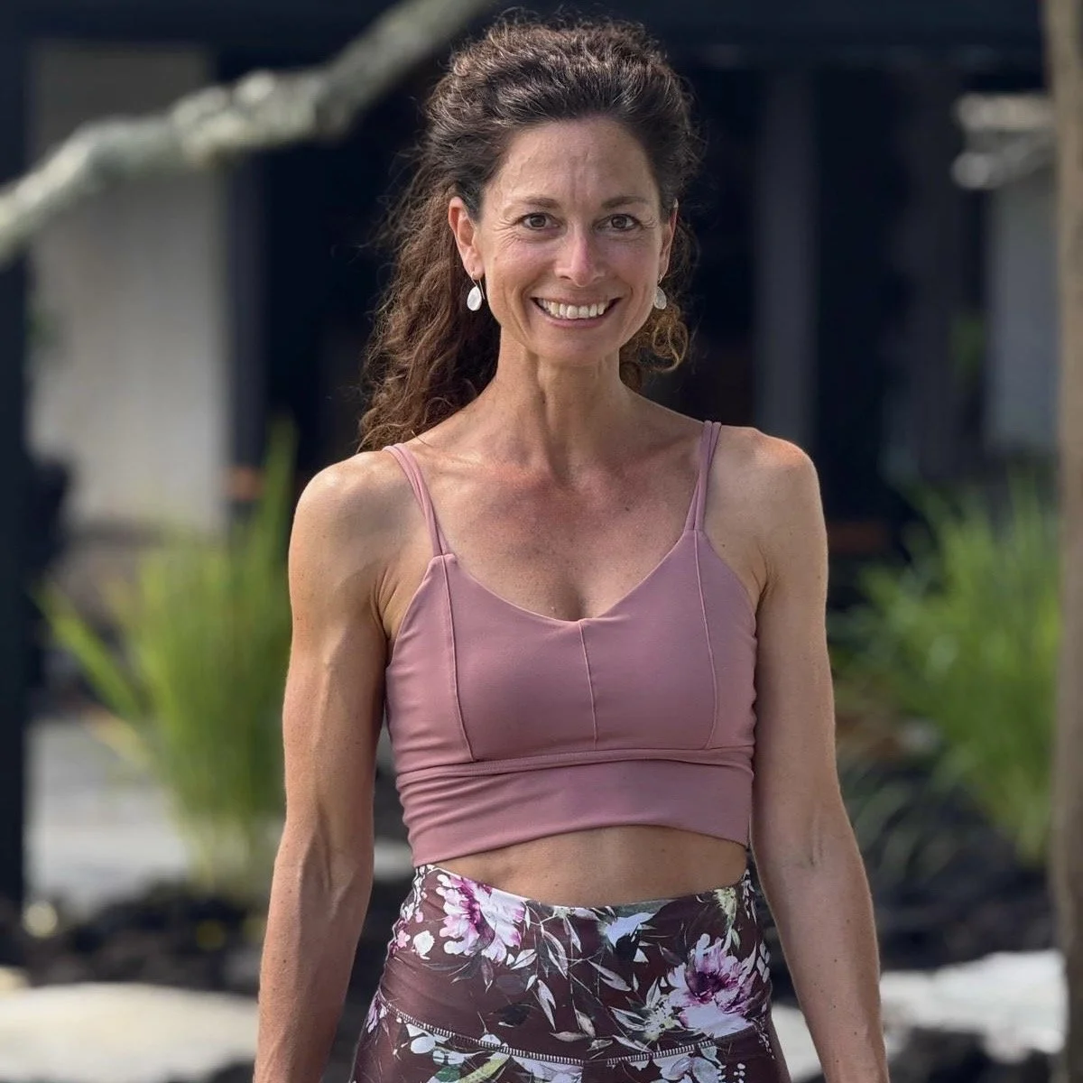 A smiling woman in a pink crop top and floral skirt standing outdoors.