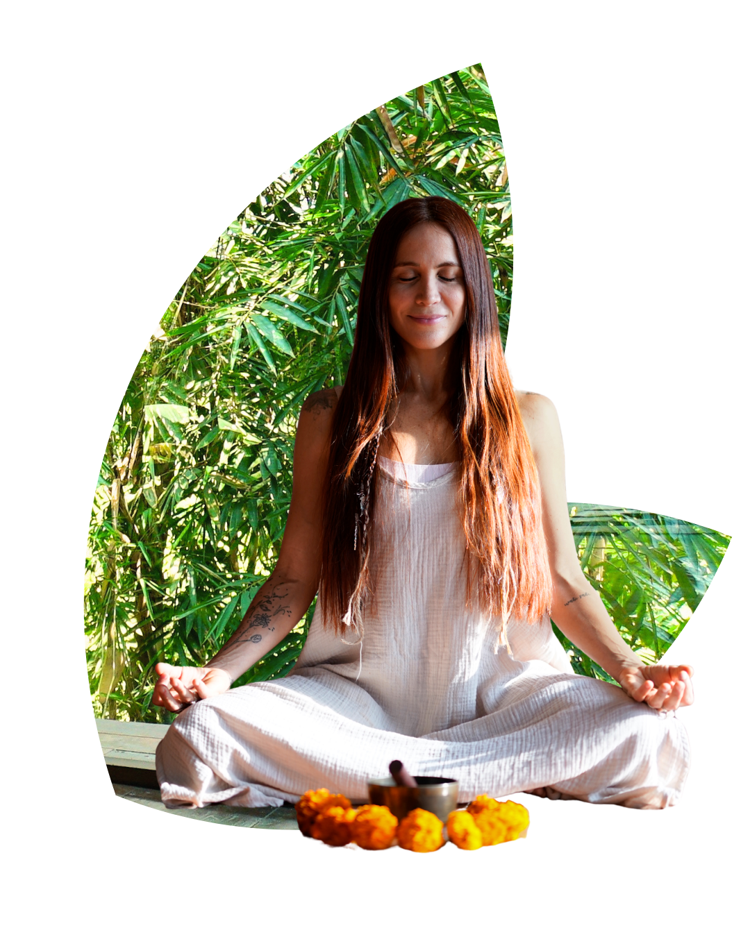 A woman in white clothing practicing meditation outdoors among green plants, with marigold flowers and a singing bowl in front of her.