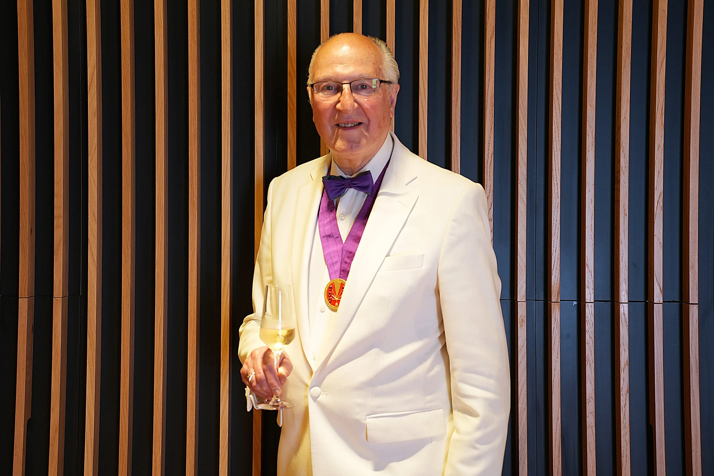 Man in tuxedo holding a champagne flute, smiling at a formal event.
