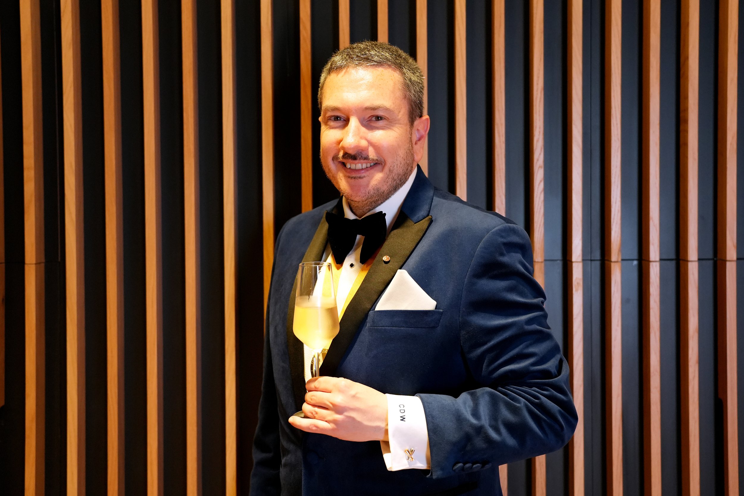 Man in a tuxedo holding a glass of champagne at a formal event