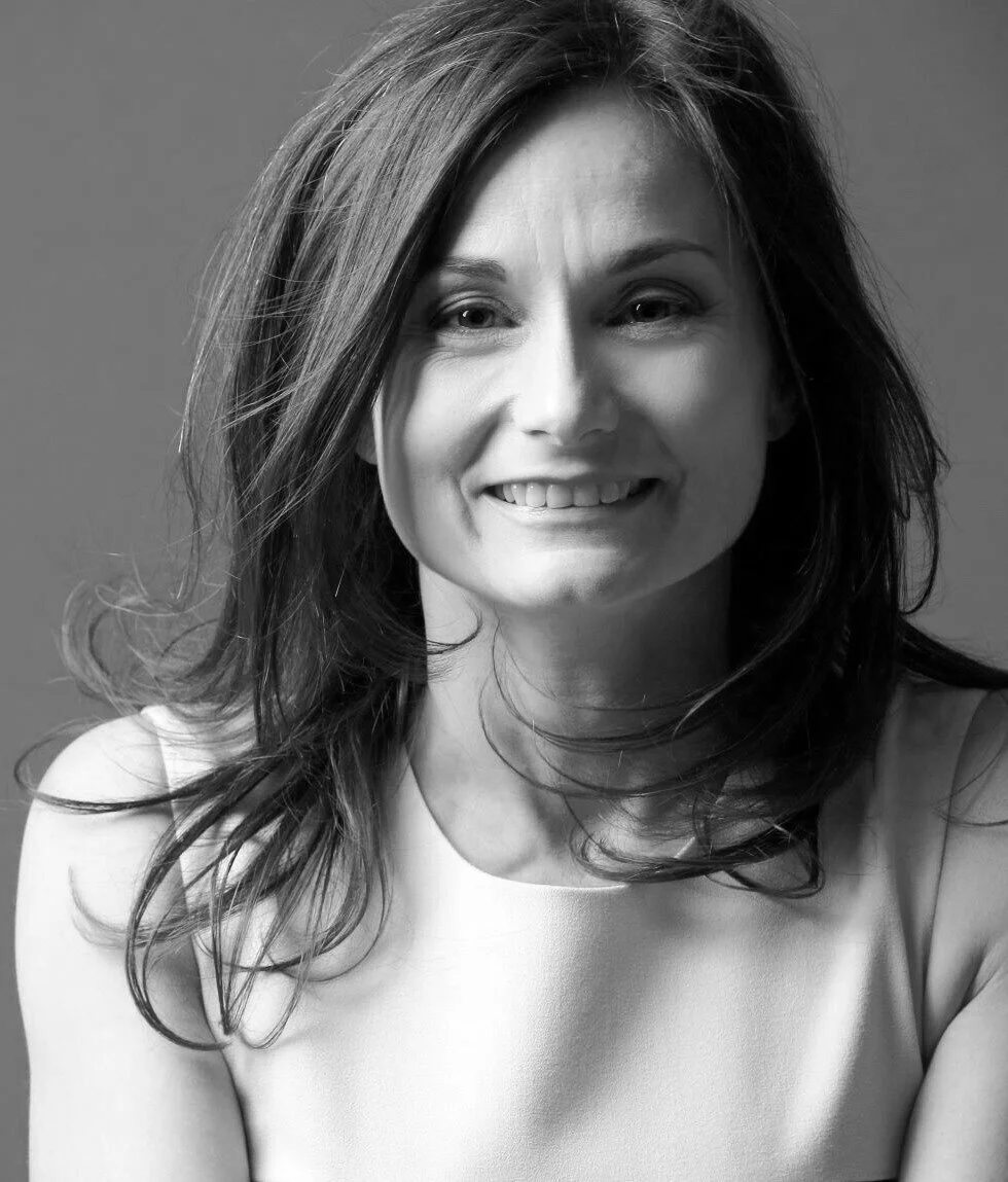 Black and white portrait of a smiling woman with shoulder-length hair, wearing a sleeveless top.