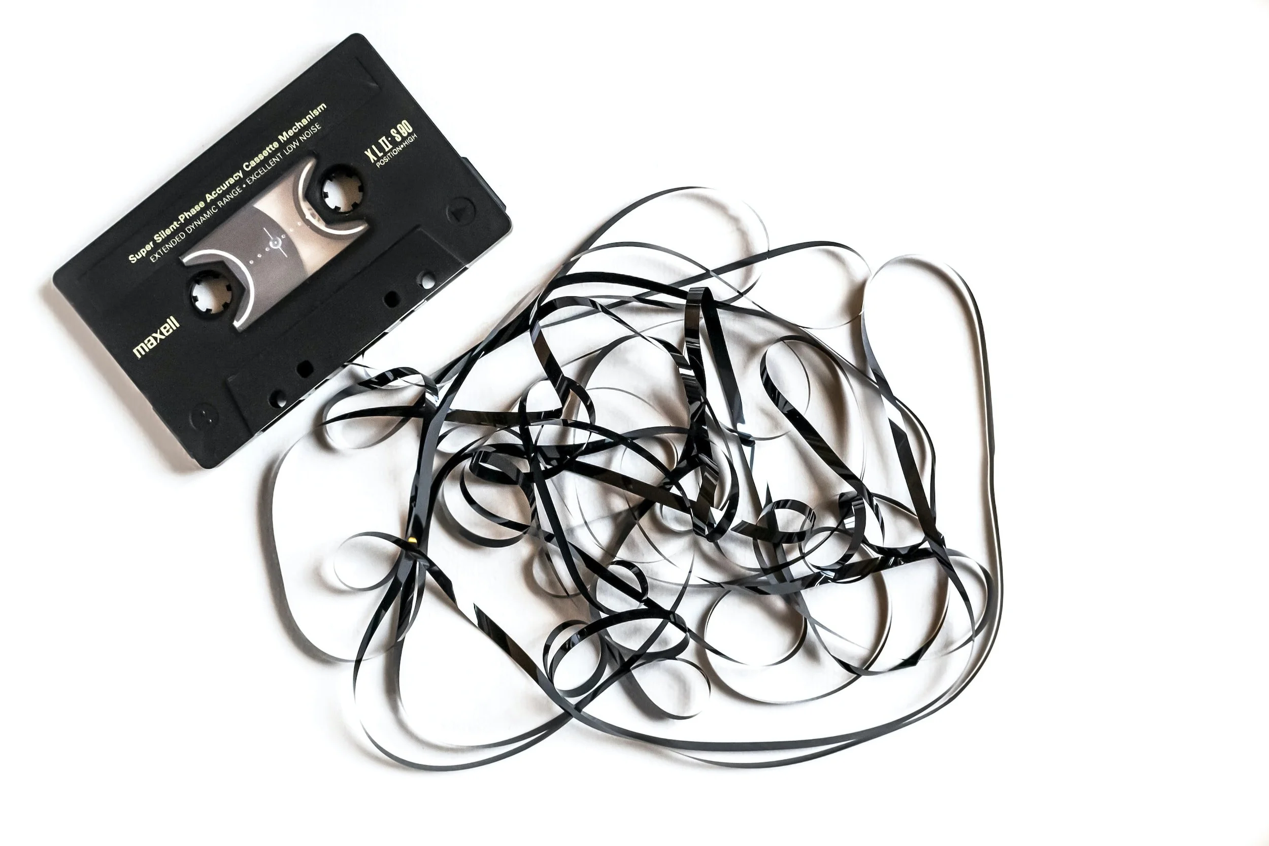 A black audio cassette tape with a tangled strip of black magnetic tape on a white background.