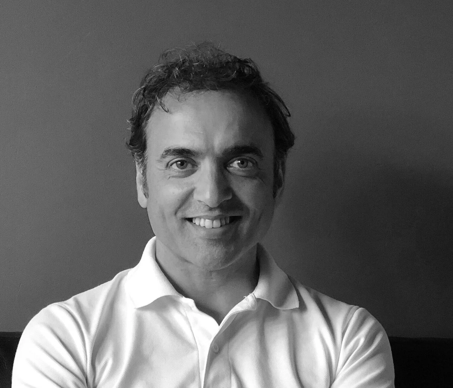 Black and white portrait of a smiling man with short curly hair wearing a white collared shirt.