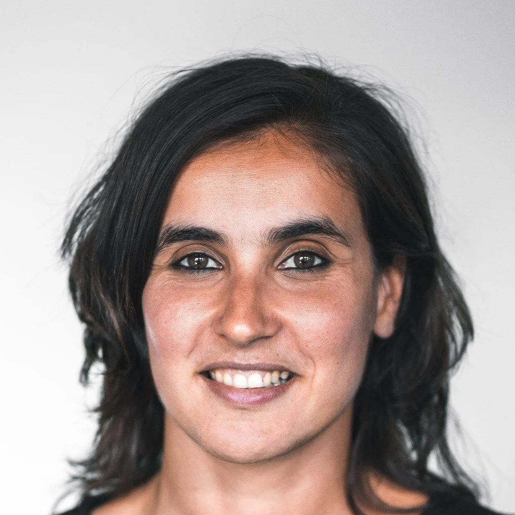 Close-up portrait of a woman with dark hair, wearing a black top, smiling, against a plain white background.