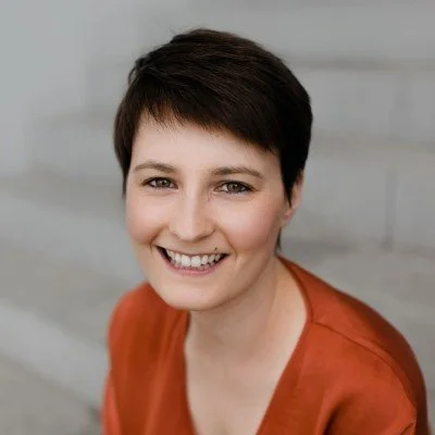 Portrait of a smiling woman with short dark hair, wearing an orange top.
