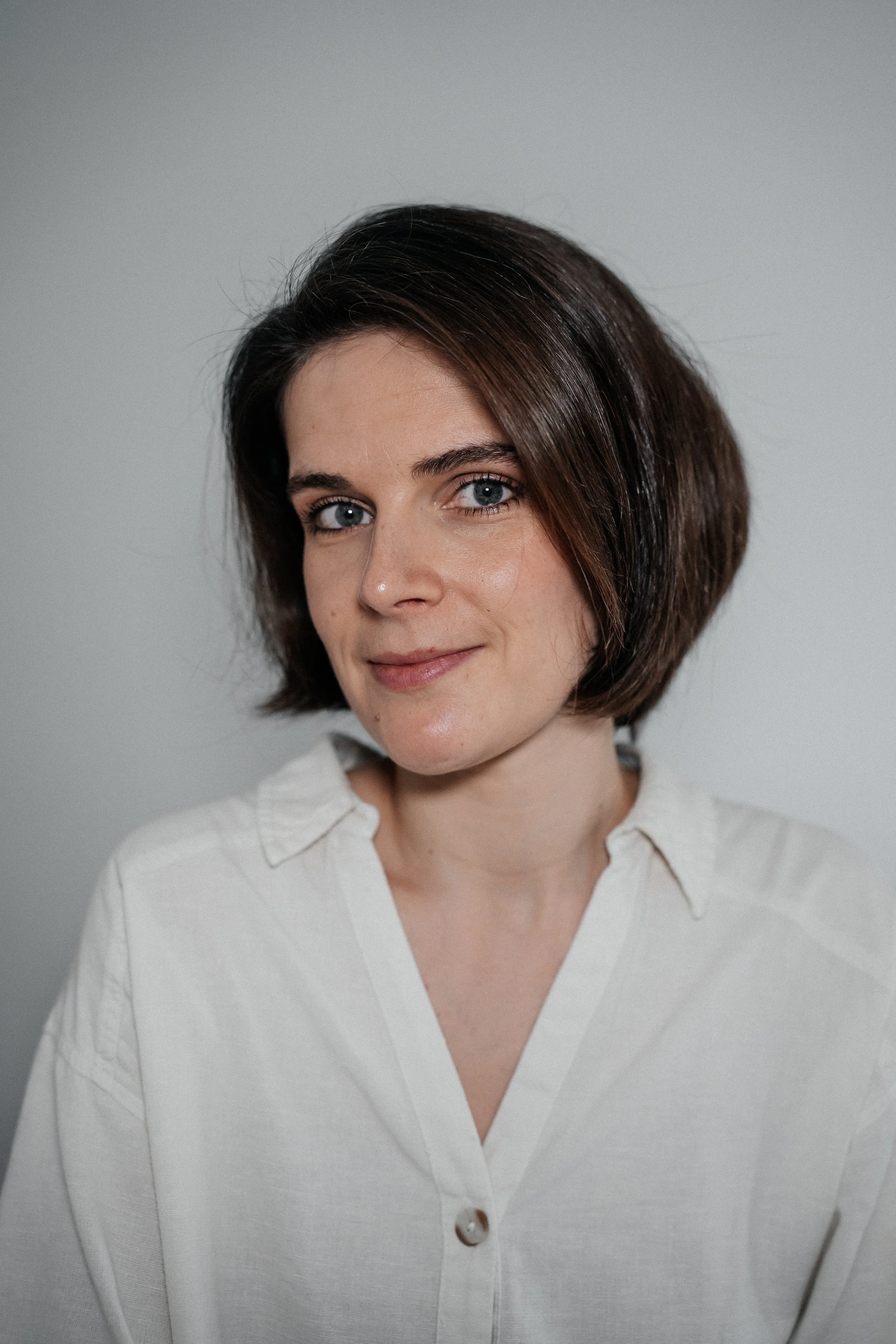 Katya Khimenets  motion designer, with short brown hair wearing a white shirt, smiling, against a plain background.