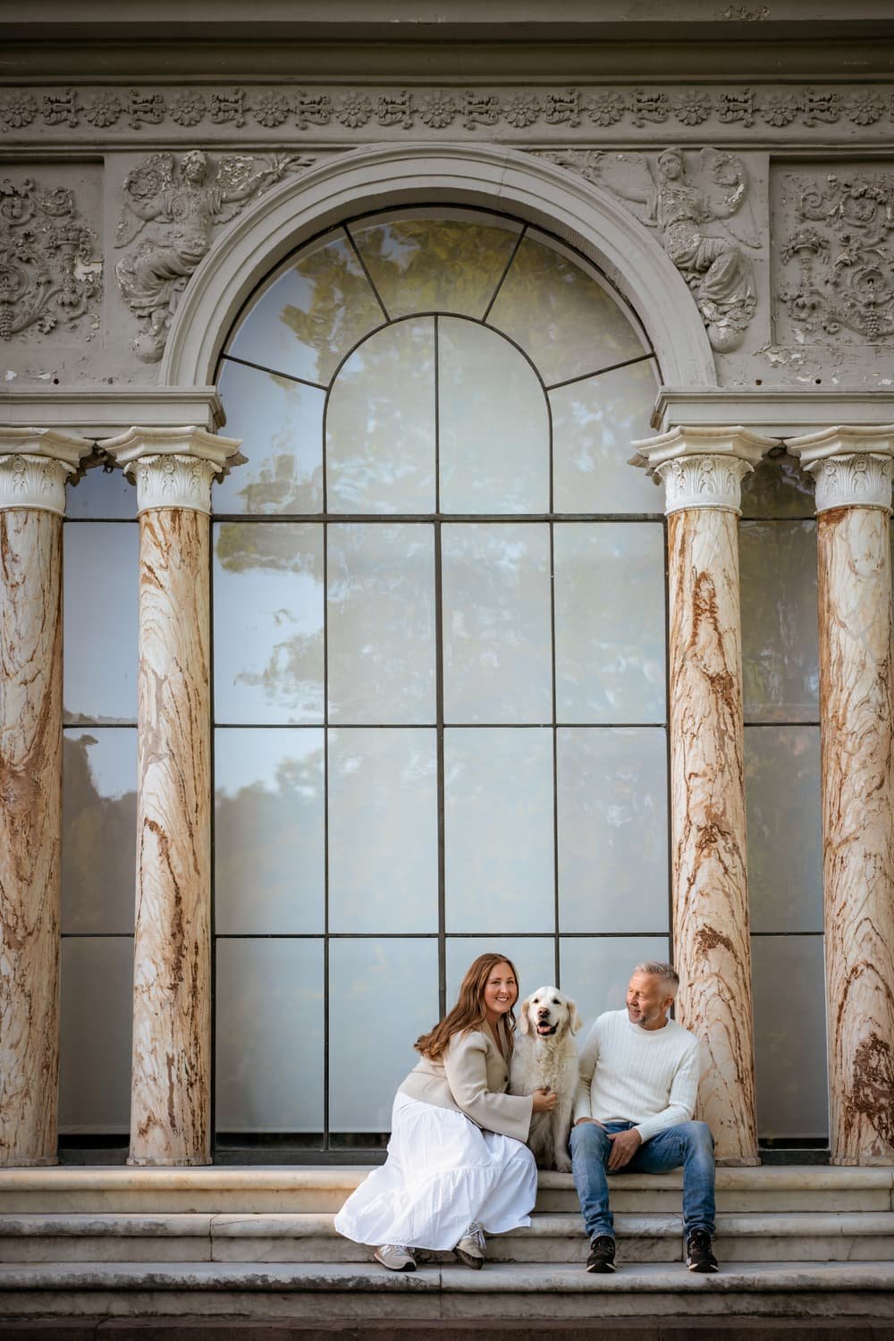 Couple and dog sitting on the steps during photo shoot in Stockholm. The woman and man are smiling, and the dog is sitting between them.