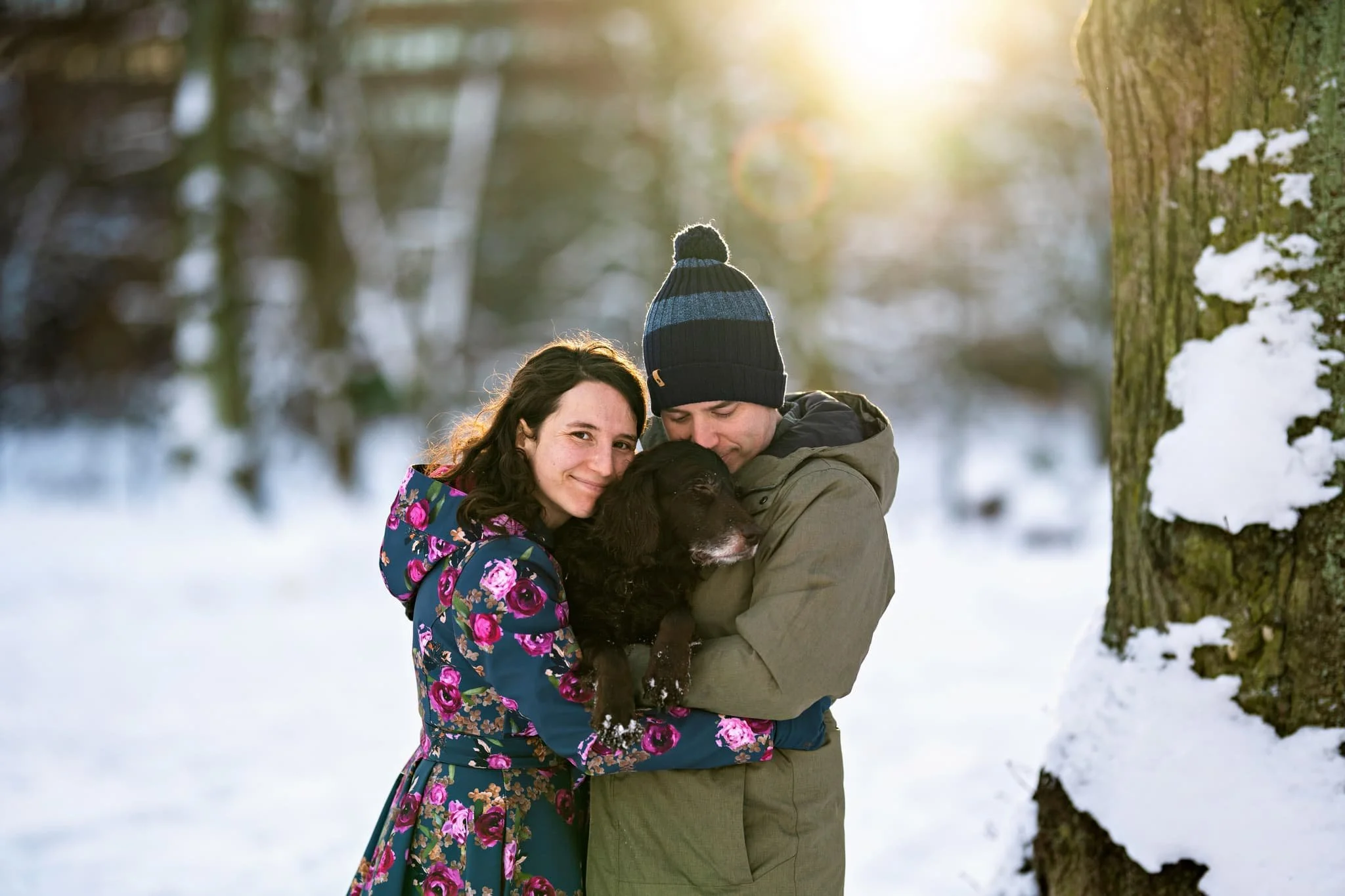 Par med en glad hund under en hundfotografering i Gustaf Adolfsparken i Stockholm, vintrig snömiljö