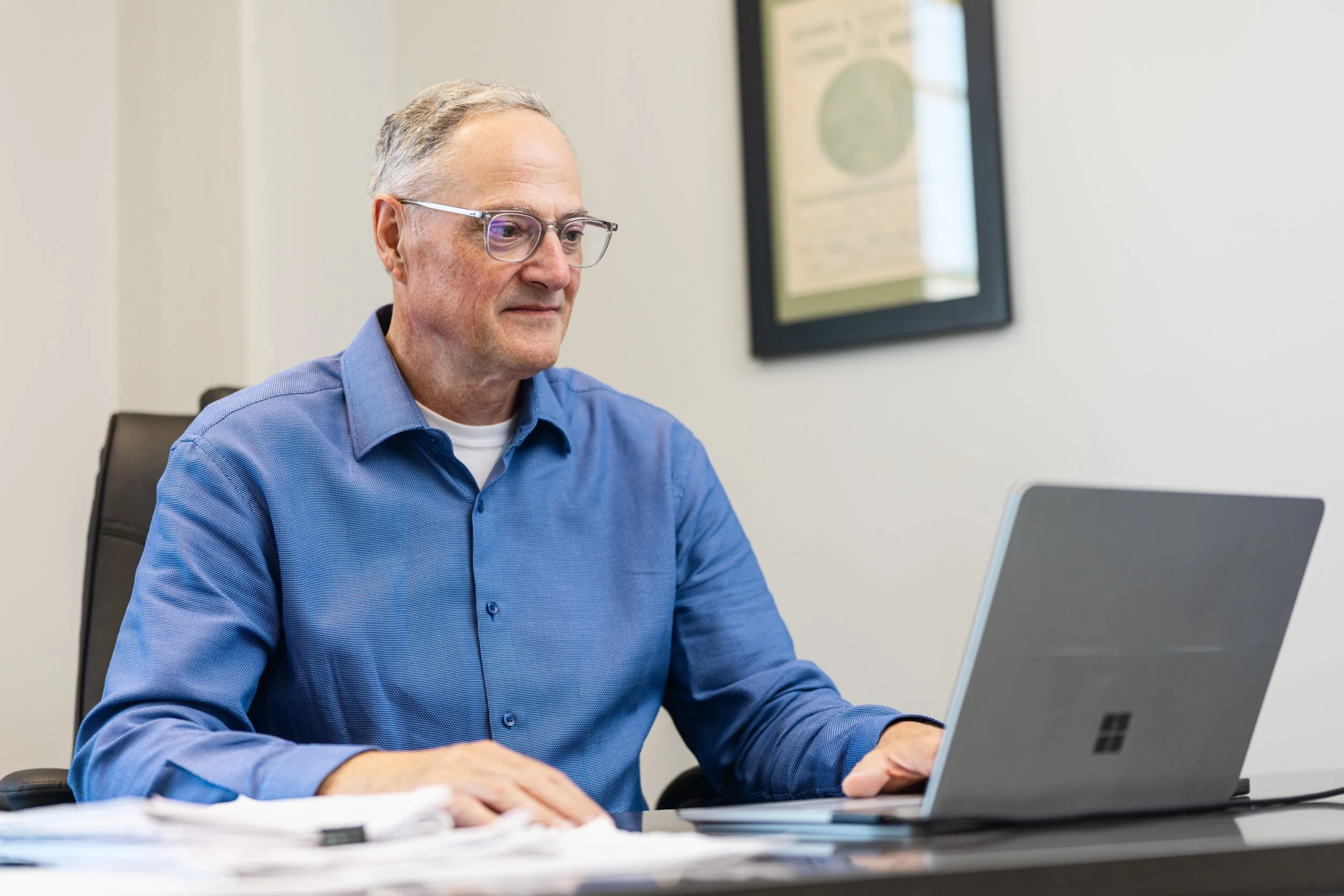 John Kerr, sitting at a desk and working on a laptop in an office setting.