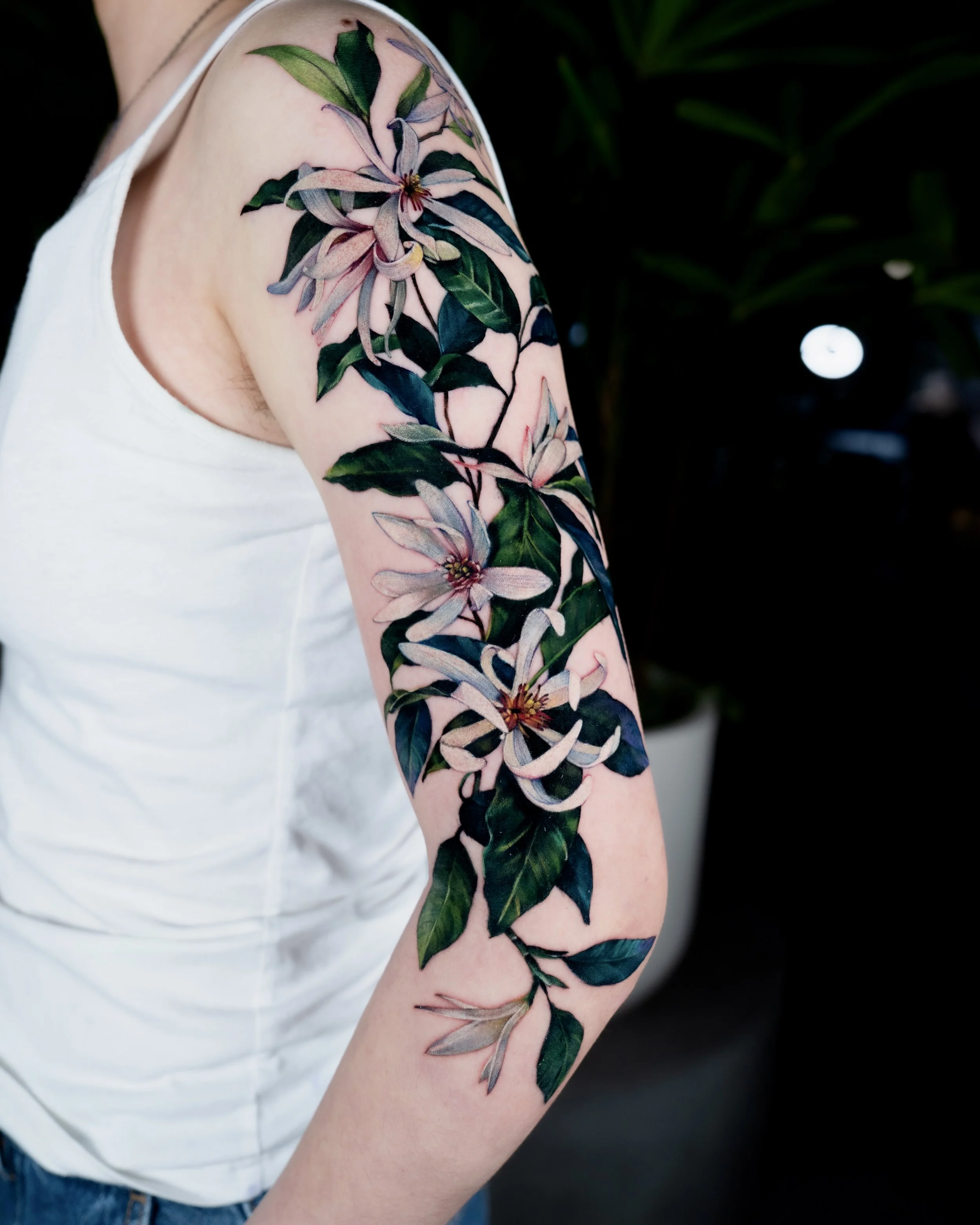 Colorful floral tattoo on person's upper arm with green leaves and pink lilies.