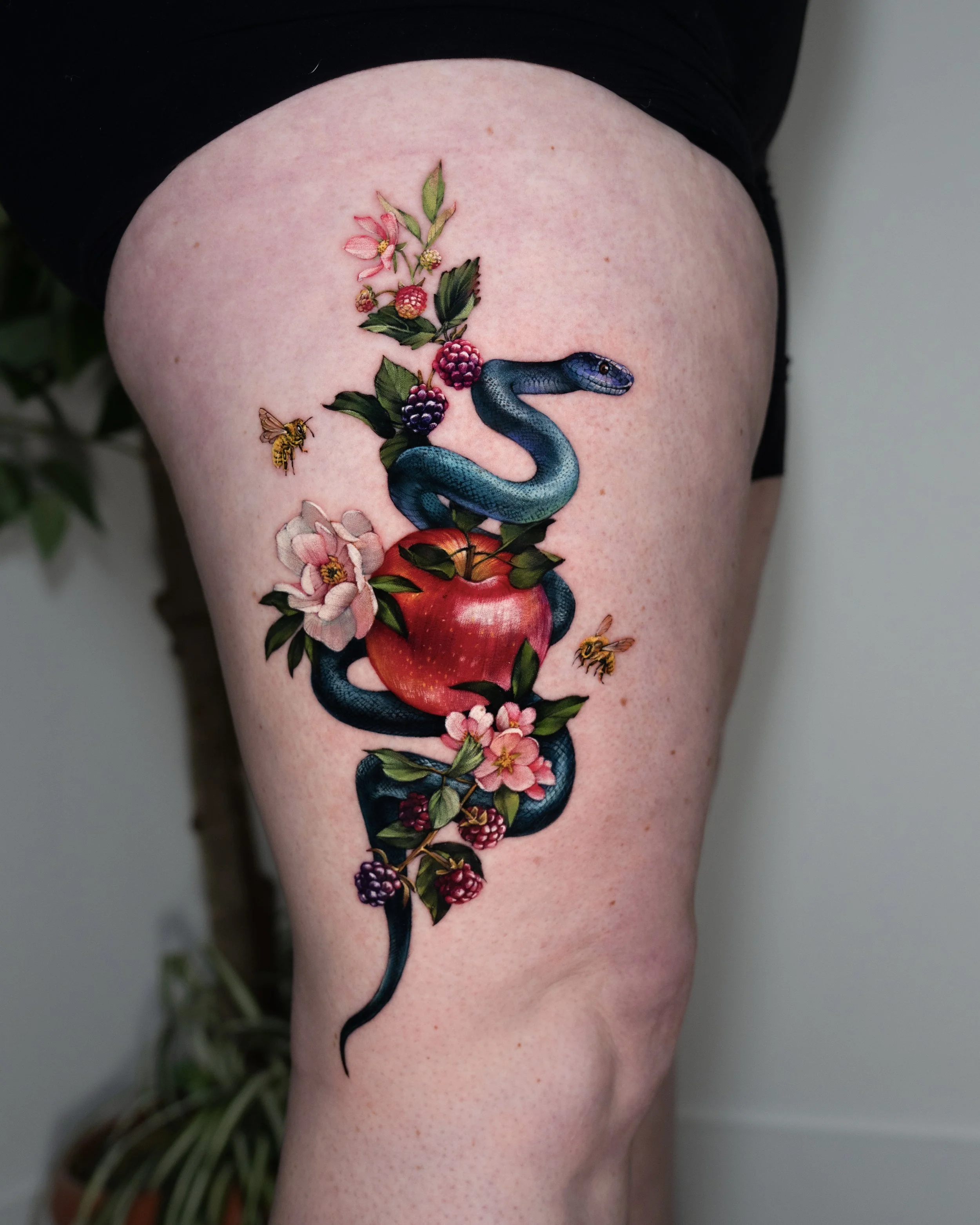 A tattoo of a snake intertwined with a branch of pink and purple berries and flowers on a person's upper arm.