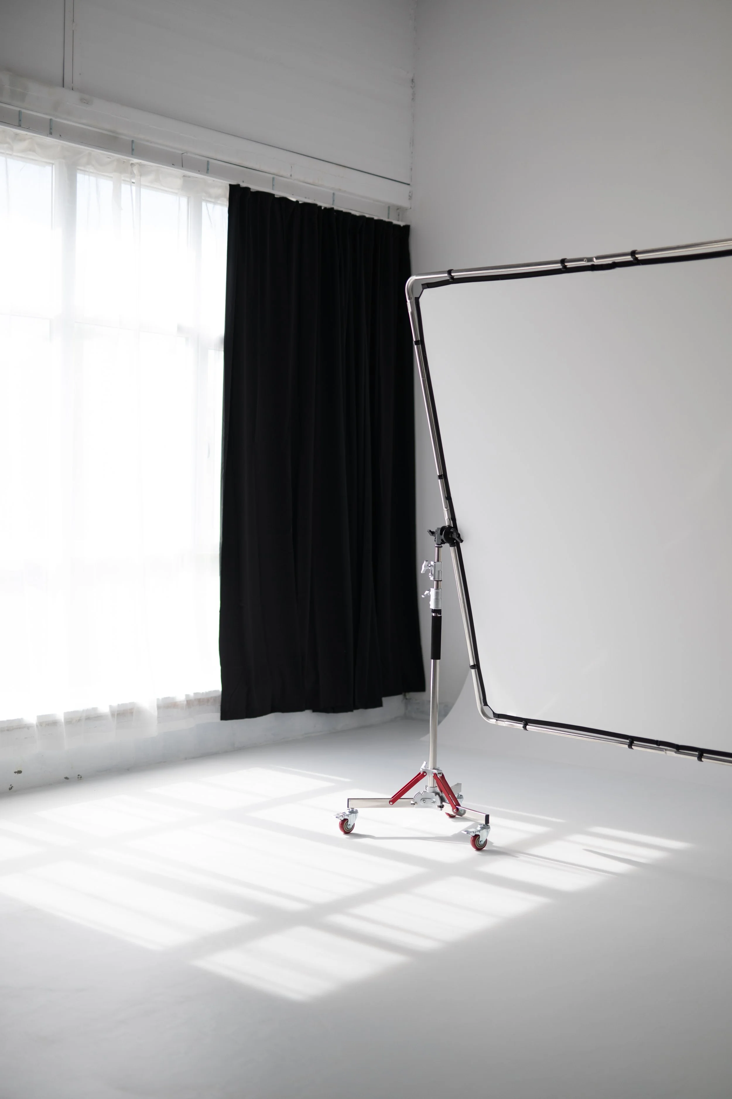  studio with white walls and floor, black curtain on window, studio light stand with a reflector or backdrop