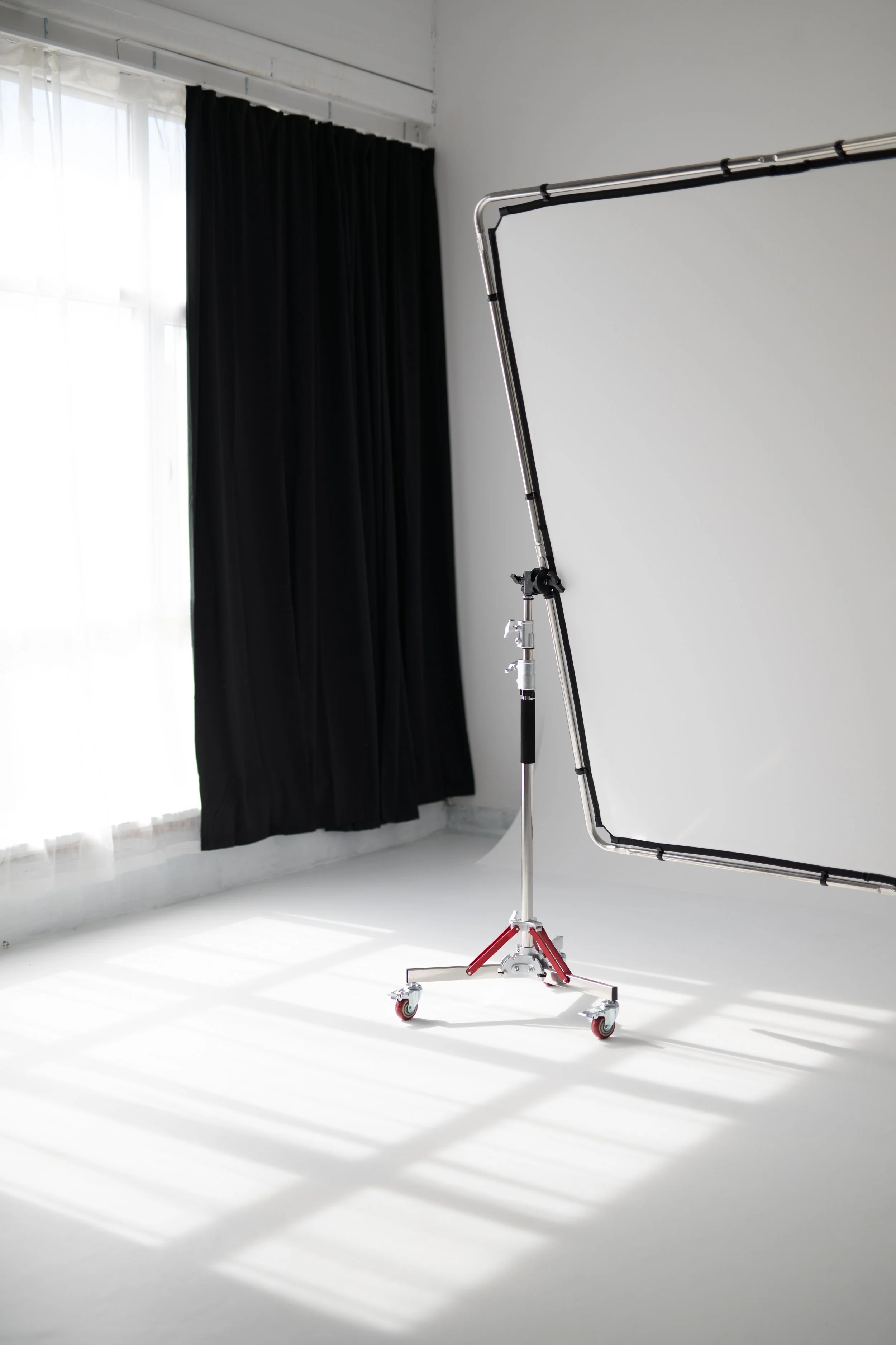 Empty photo studio with a white backdrop, a black curtain, and a professional lighting stand casting shadows on the floor.