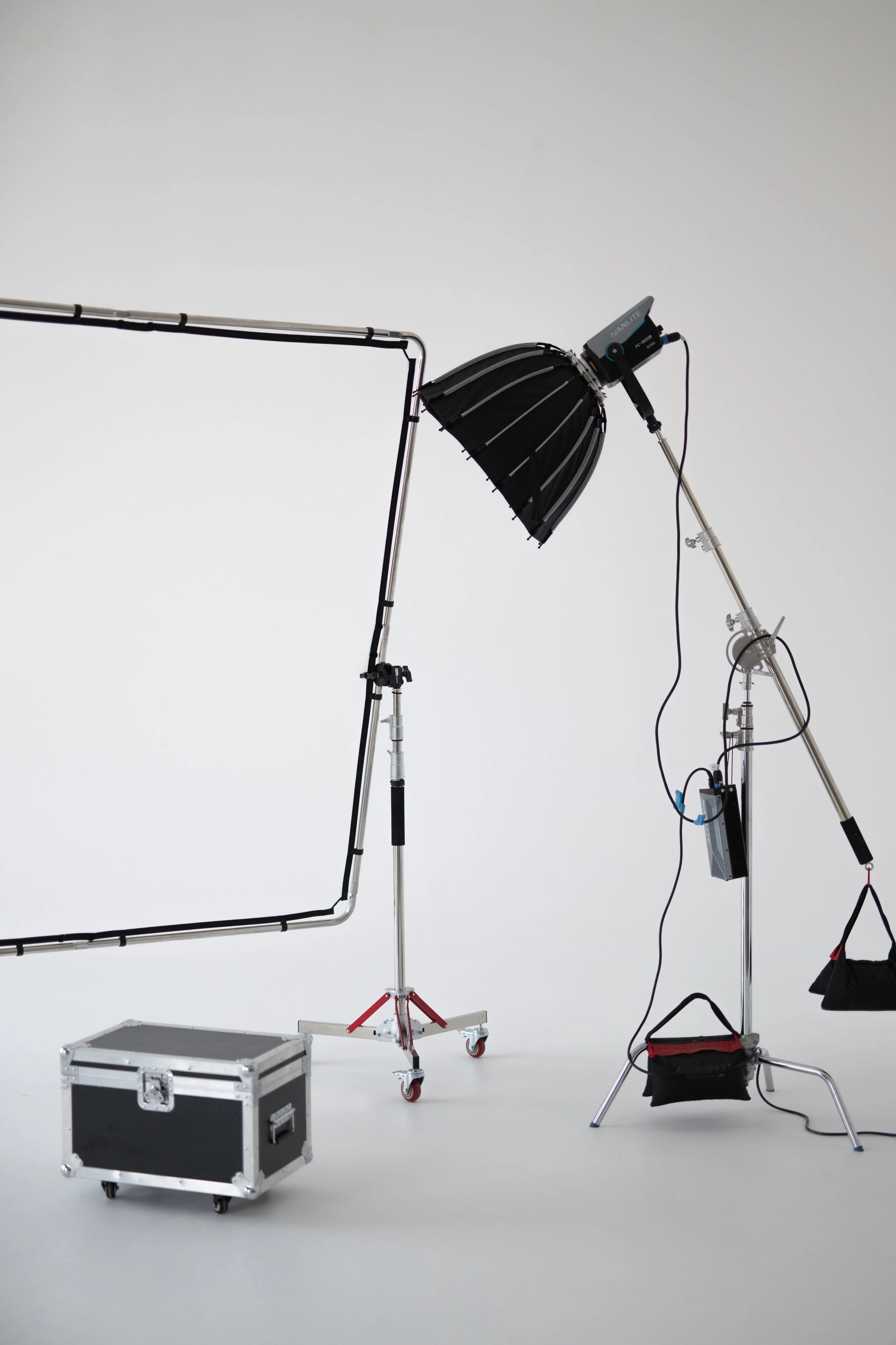 Photography lighting equipment setup including a large softbox light, a reflector, and various stands and cases against a plain white background.