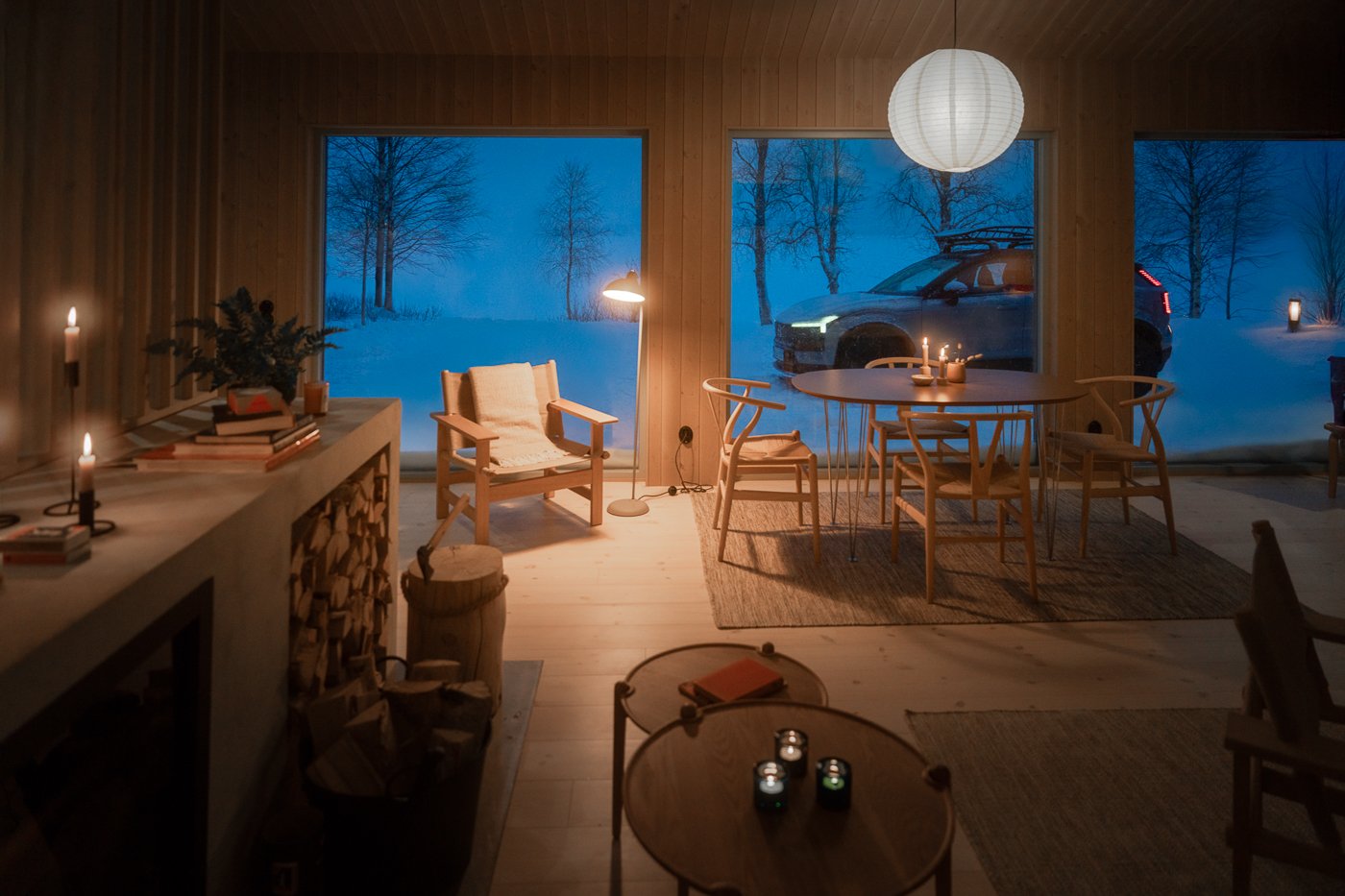 Cozy interior of a wooden house living room with large windows showing snow-covered landscape, car parked outside, decorated with candles and warm lighting.