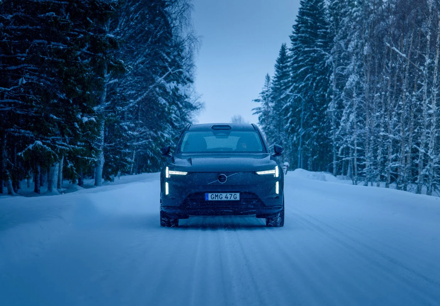 A black SUV driving on a snow-covered road through a winter forest with snow on the trees.