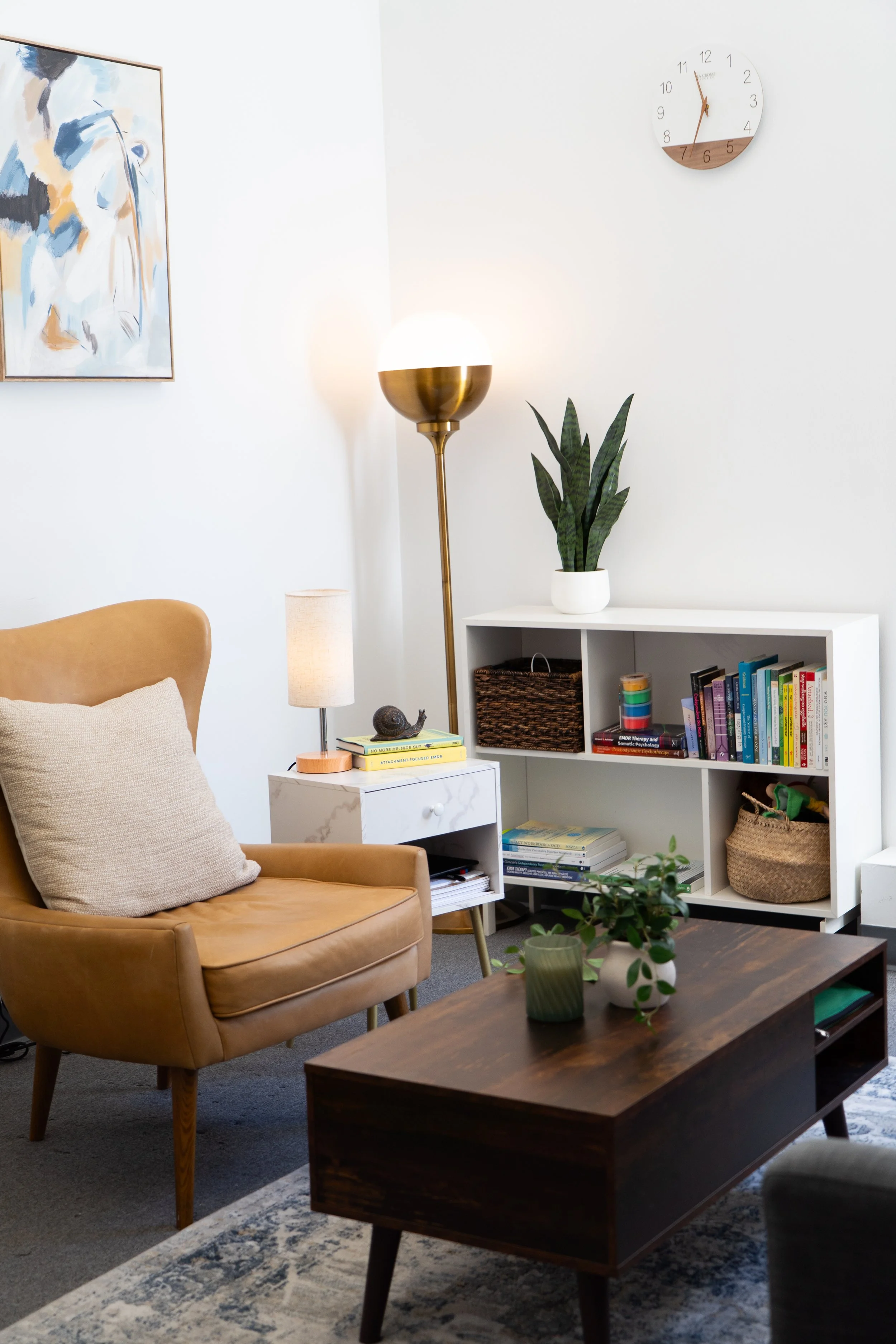 Bright inviting counseling office with brass floor lamp, tan arm chair and wooden coffee table.