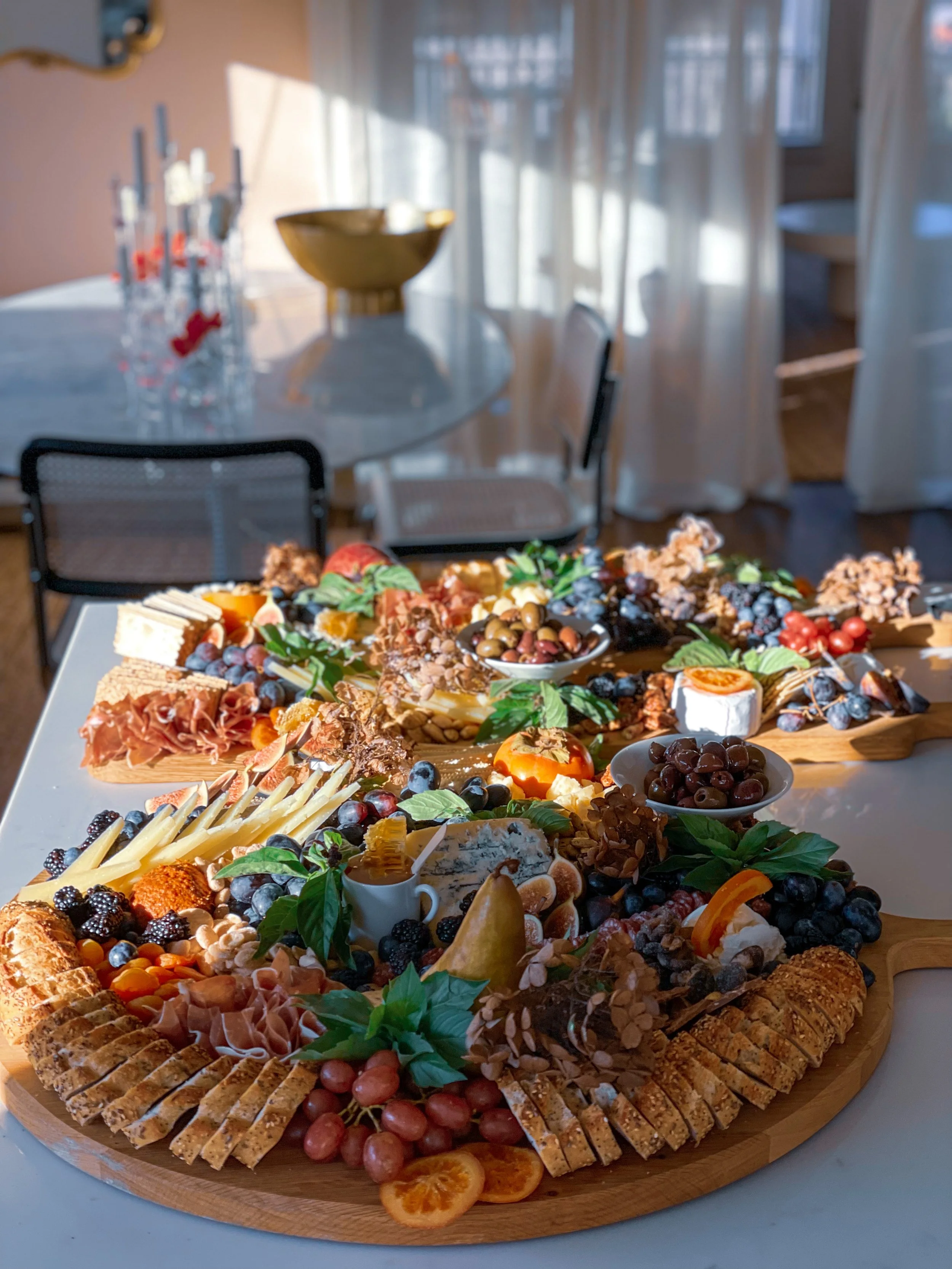 A large charcuterie board displaying a variety of meats, cheeses, fruits, nuts, and crackers, arranged on a wooden table with a bowl of olives and decorative greenery.