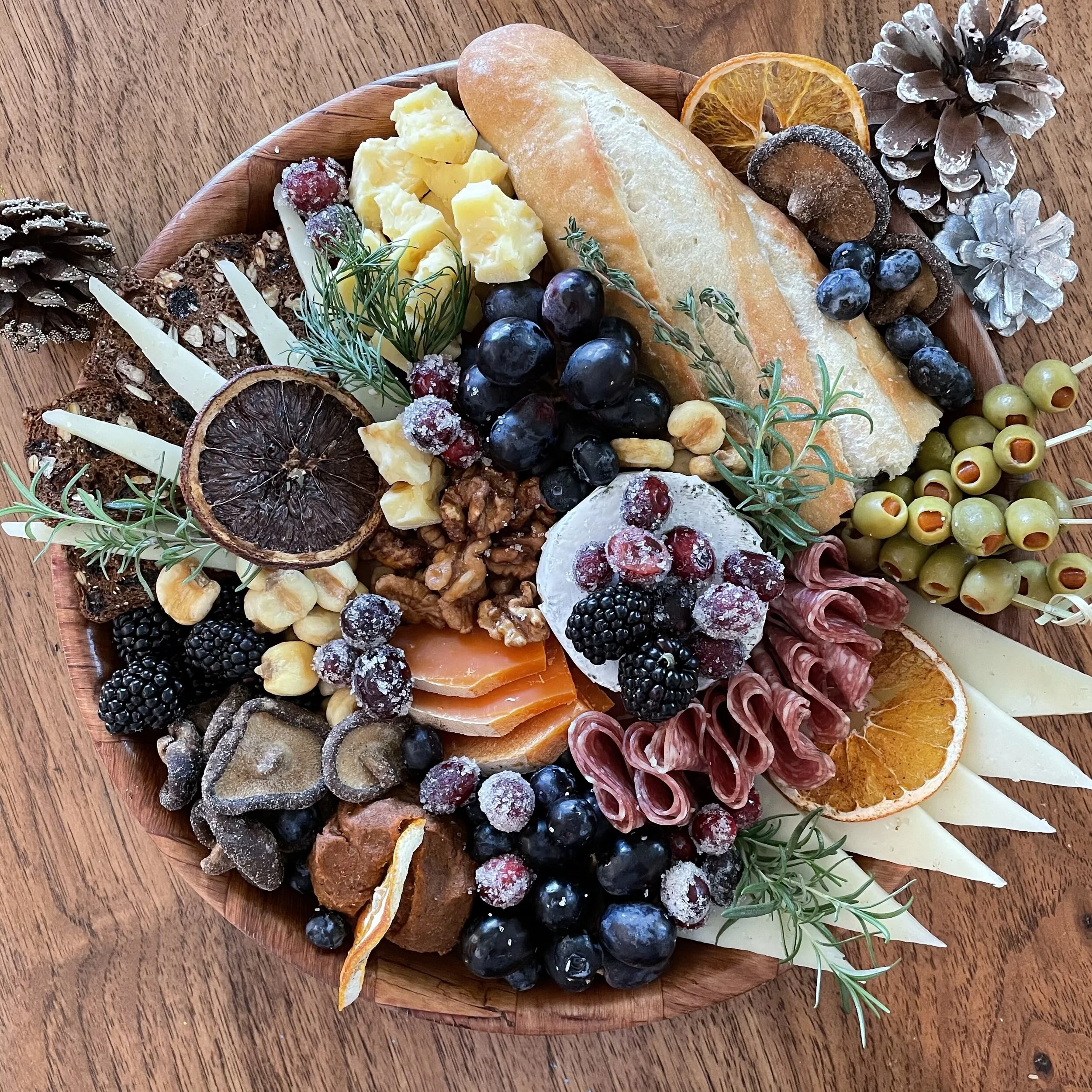 Charcuterie board with bread, cheese, nuts, berries, olives, dried fruit, and sliced meat.