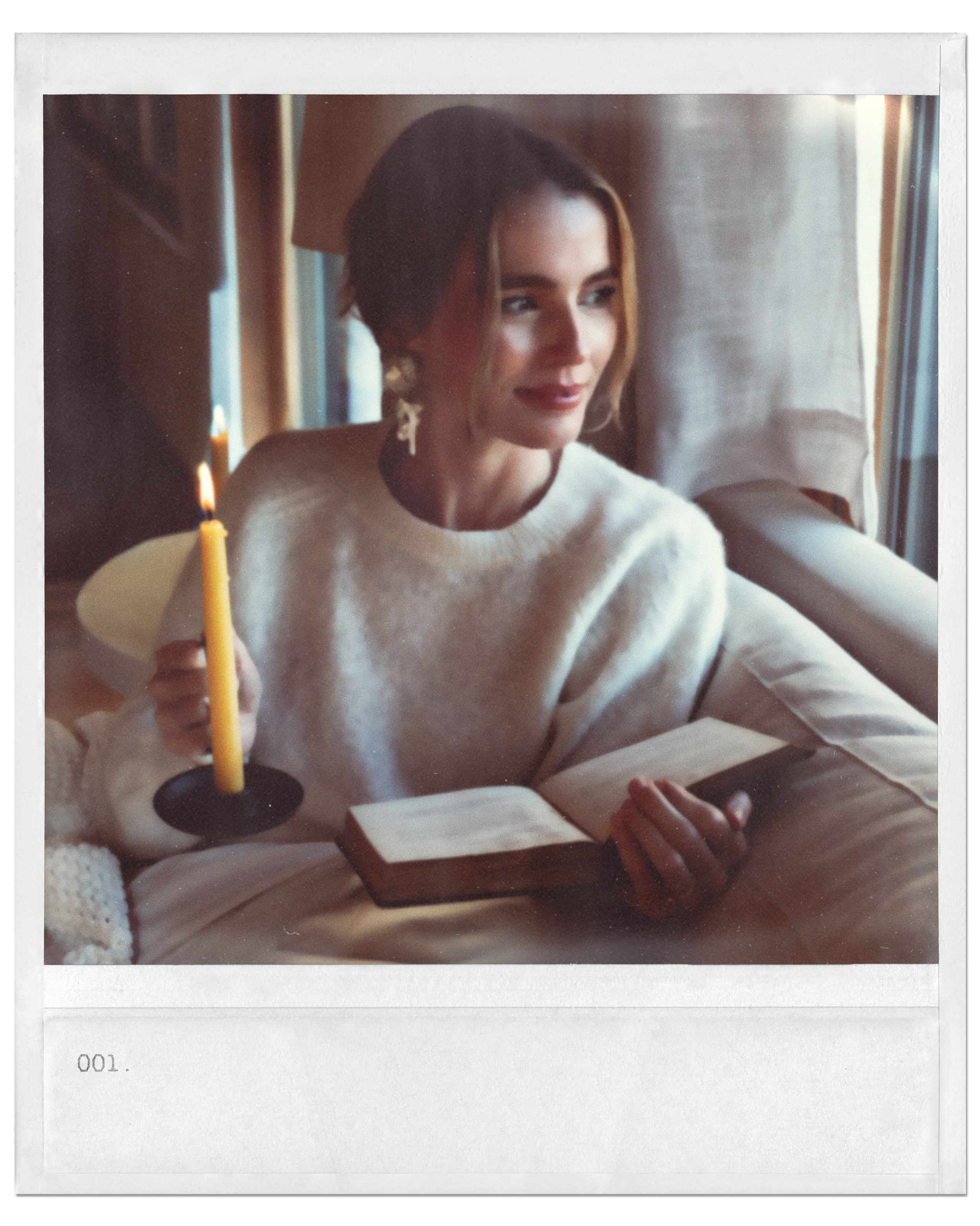 woman holding a candle and book looking out a window