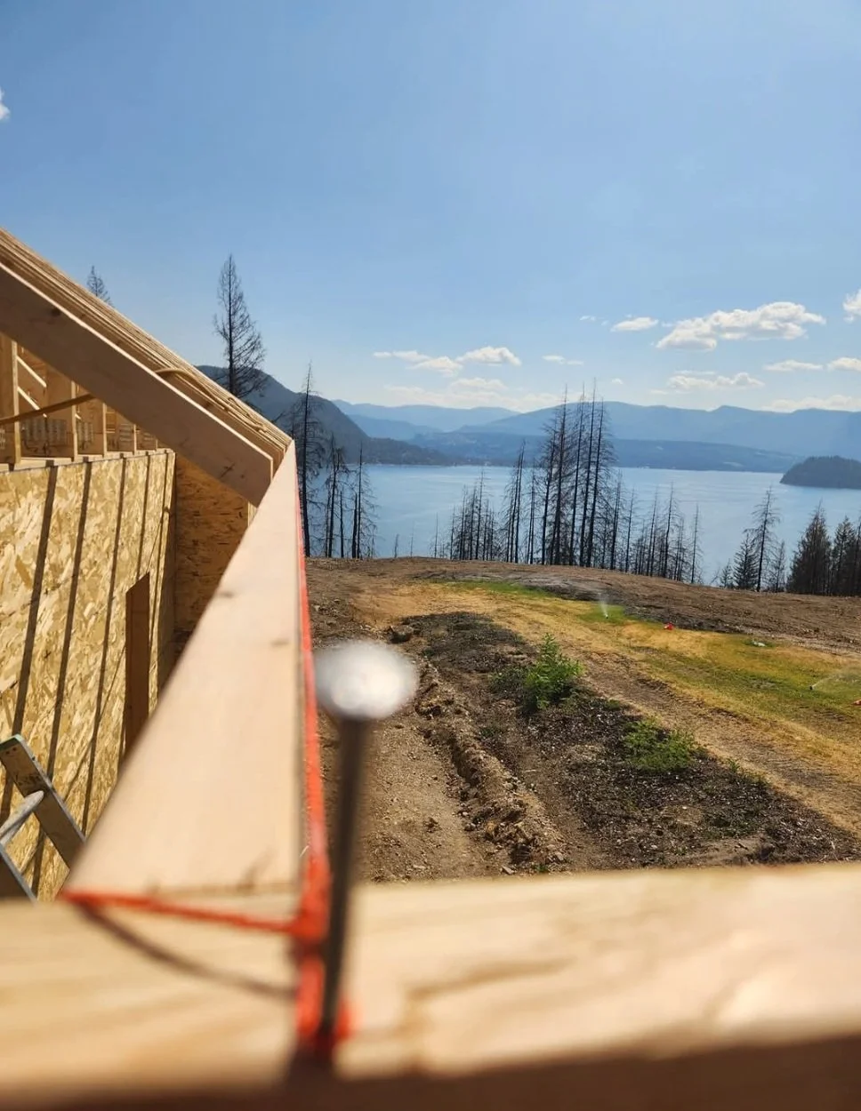 View from a construction site showing a lake surrounded by mountains and trees, with a partly built wooden structure in the foreground.