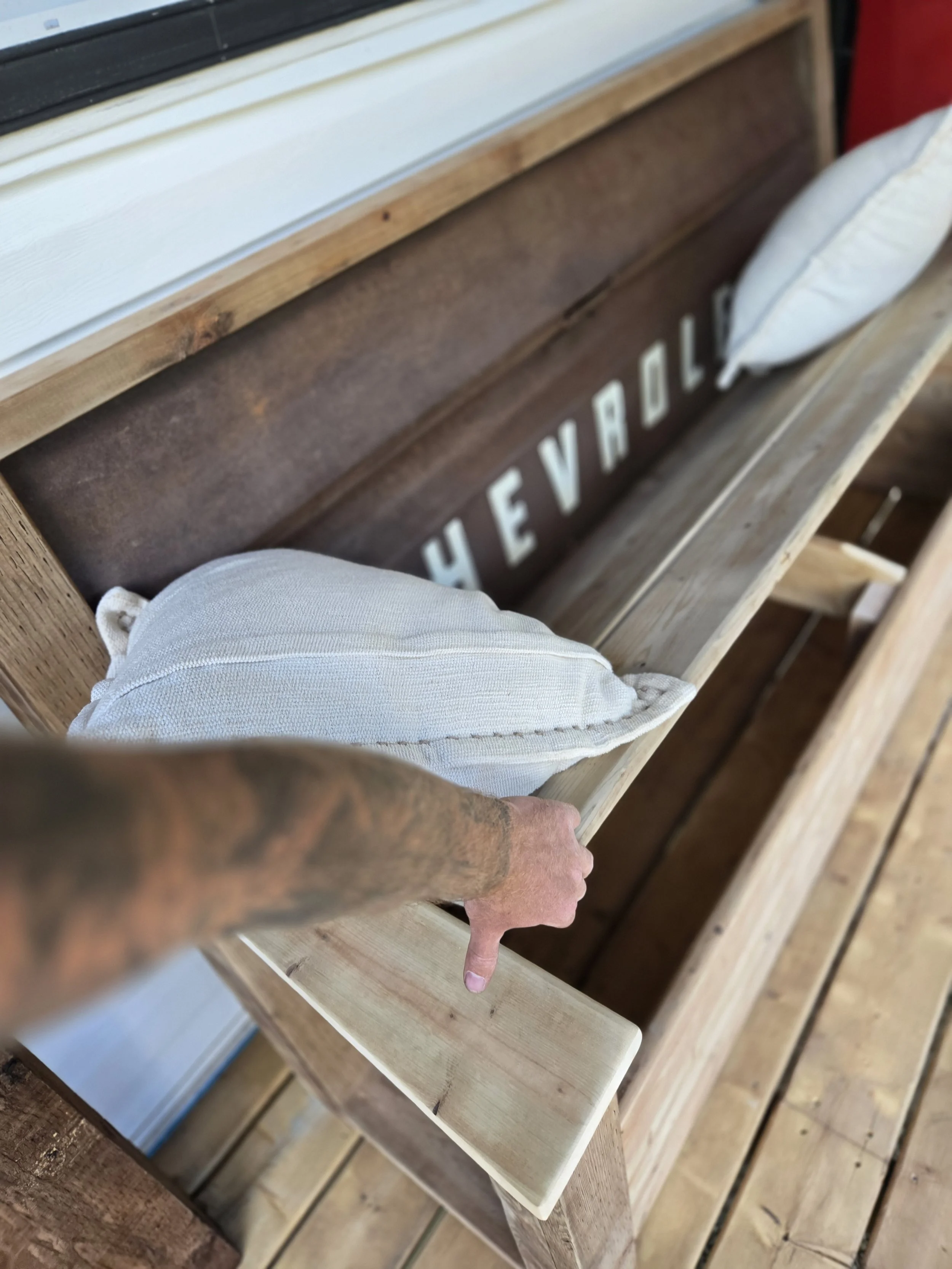 The image shows a wooden shelf with a sign that reads "HEY VARD" and a white pillow placed on the right side of the shelf.