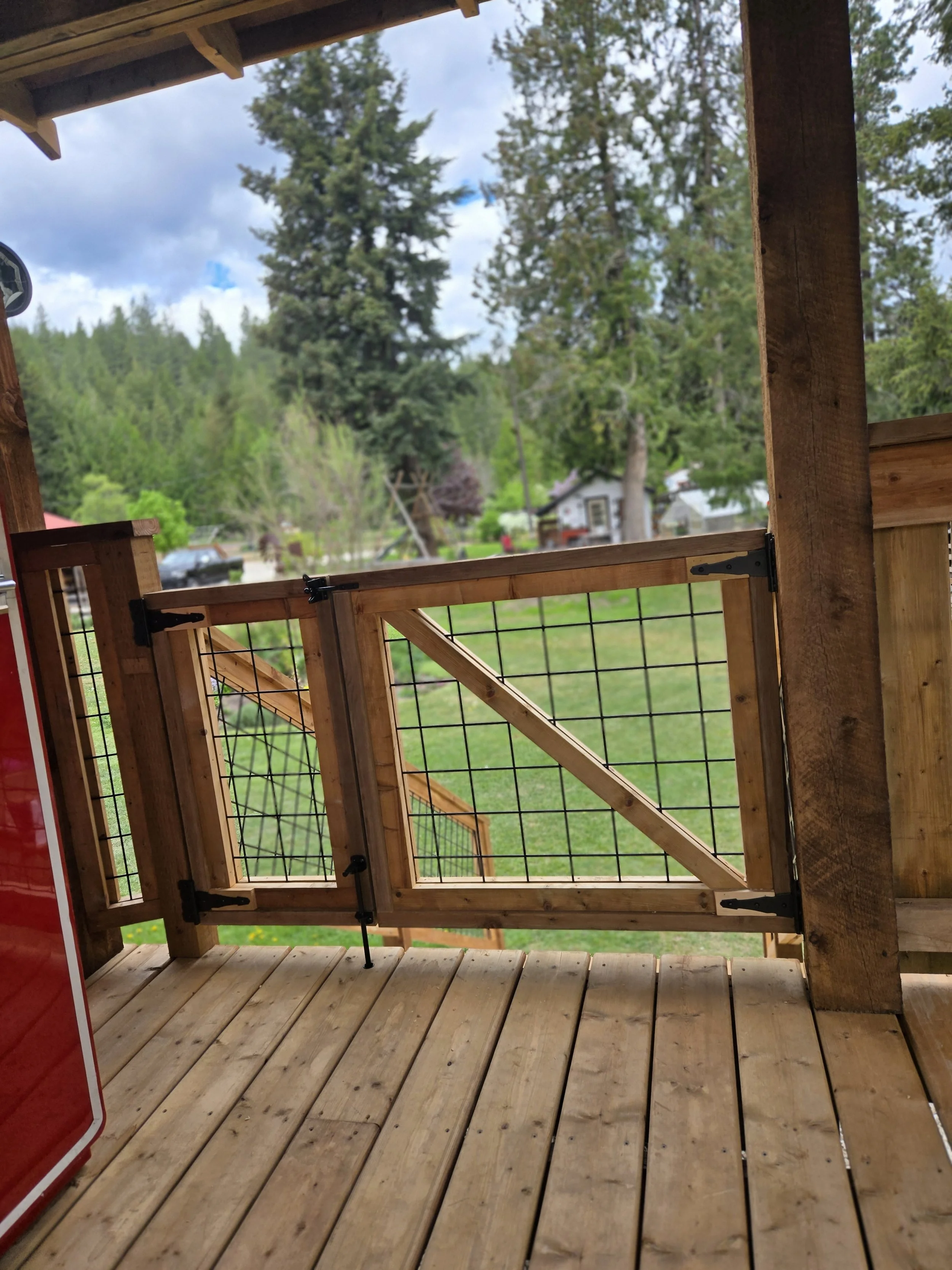 Wooden porch with railing, overlooking green trees and houses in the background on a cloudy day.