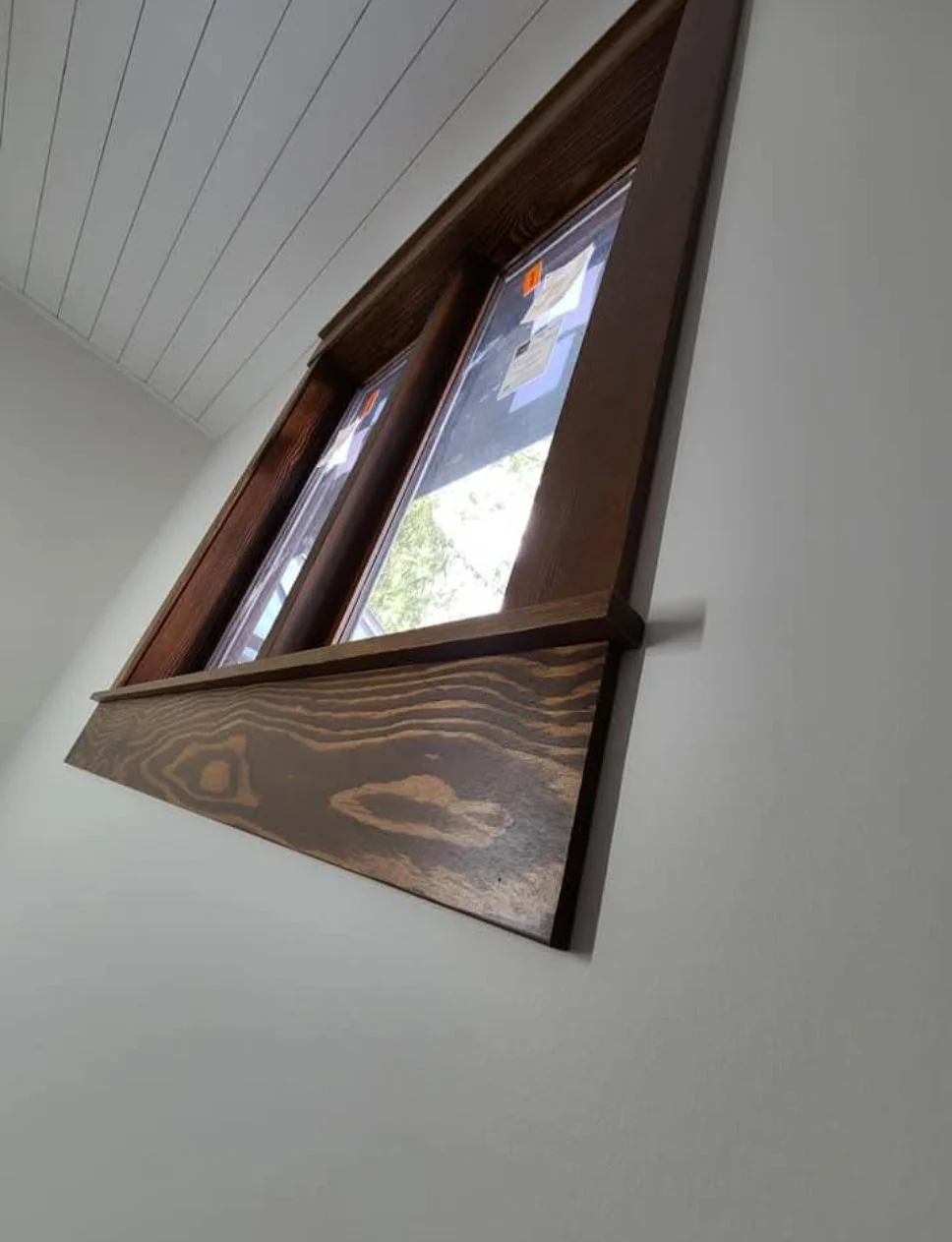 Close-up of a wooden window frame with two glass panes, mounted on a white wall, with sunlight shining through the window.