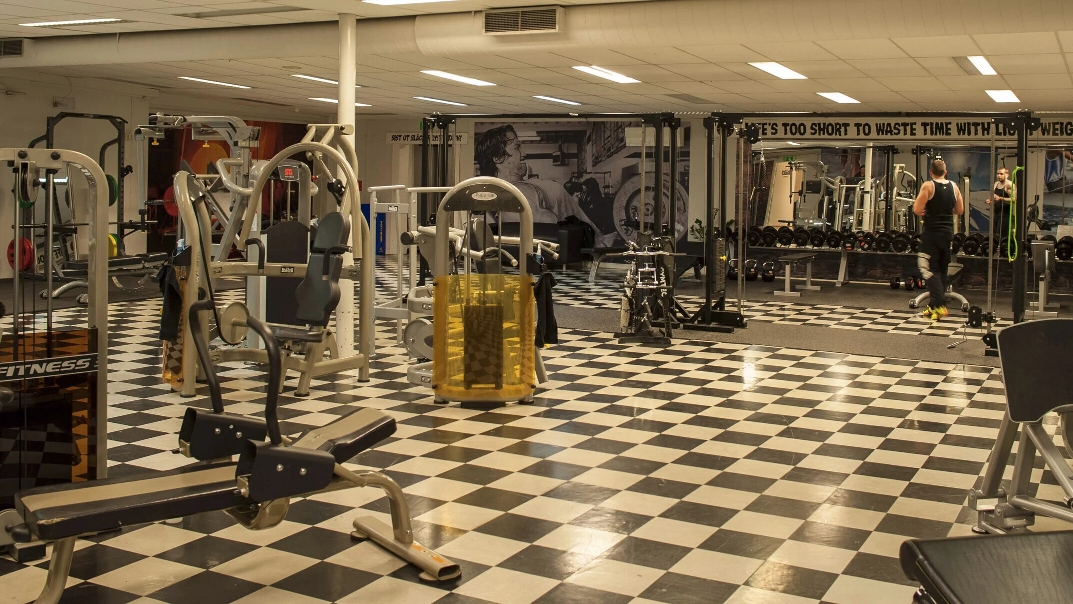 Gymlokal med maskiner och hantlar och Arnold på väggen