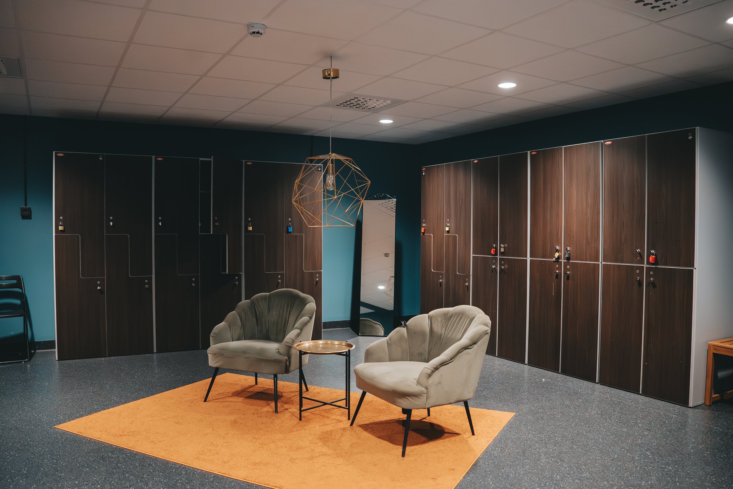 Mysigt och inbjudande omklädningsrum i varma färger med bastu, skåp och fåtöljer.