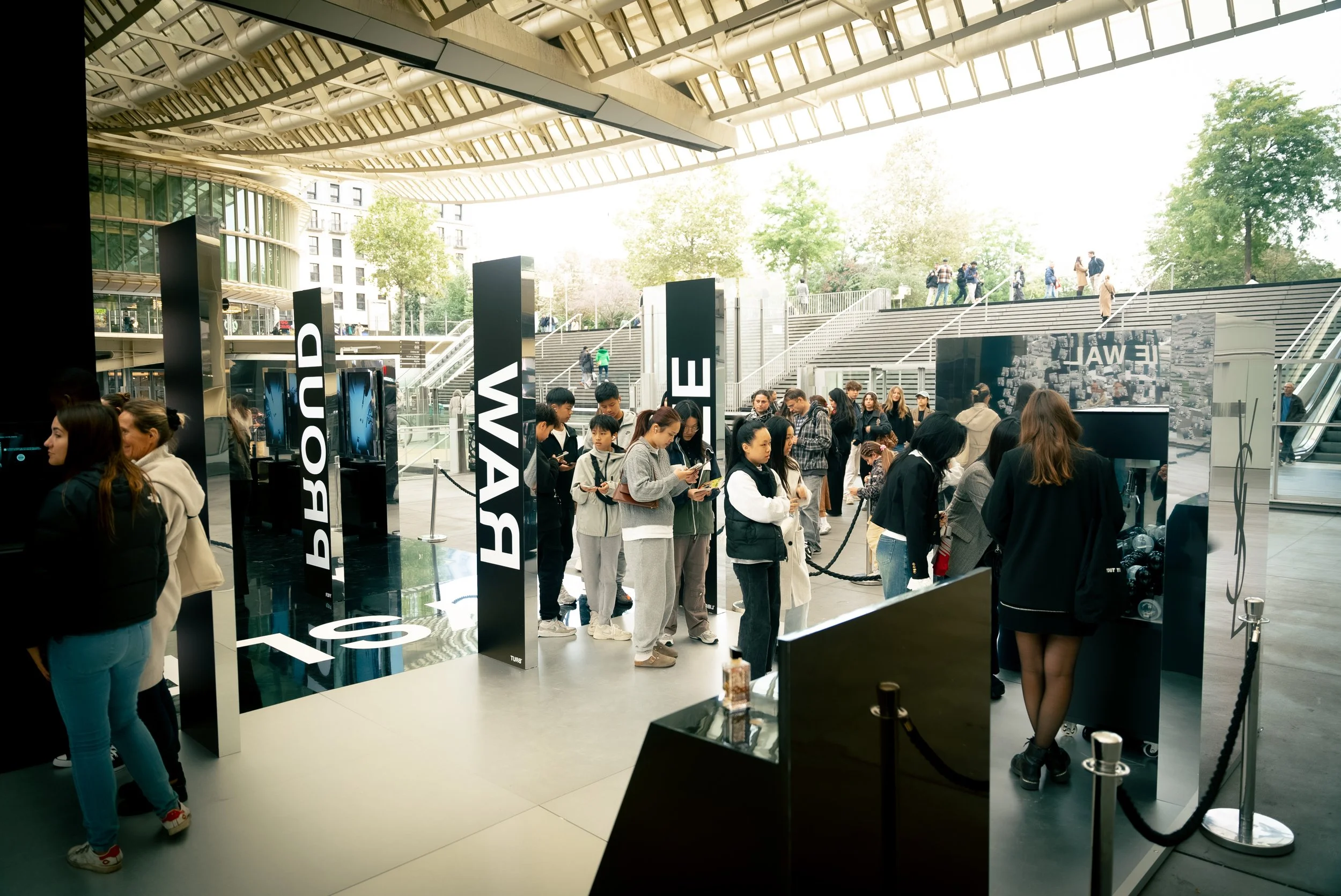 Une file d'attente de personnes à un stand d'exposition dans un bâtiment moderne avec des arbres visibles à l'extérieur.