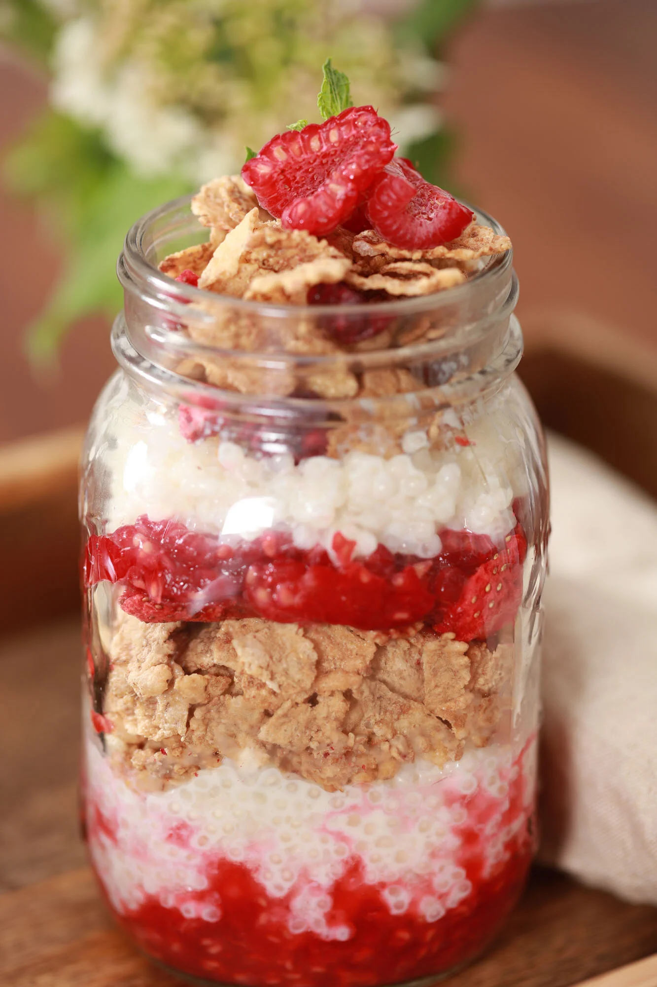 Un pot en verre contenant une couche de fraises, muesli, riz soufflé et lait, garni de fraises fraîches et de muesli.