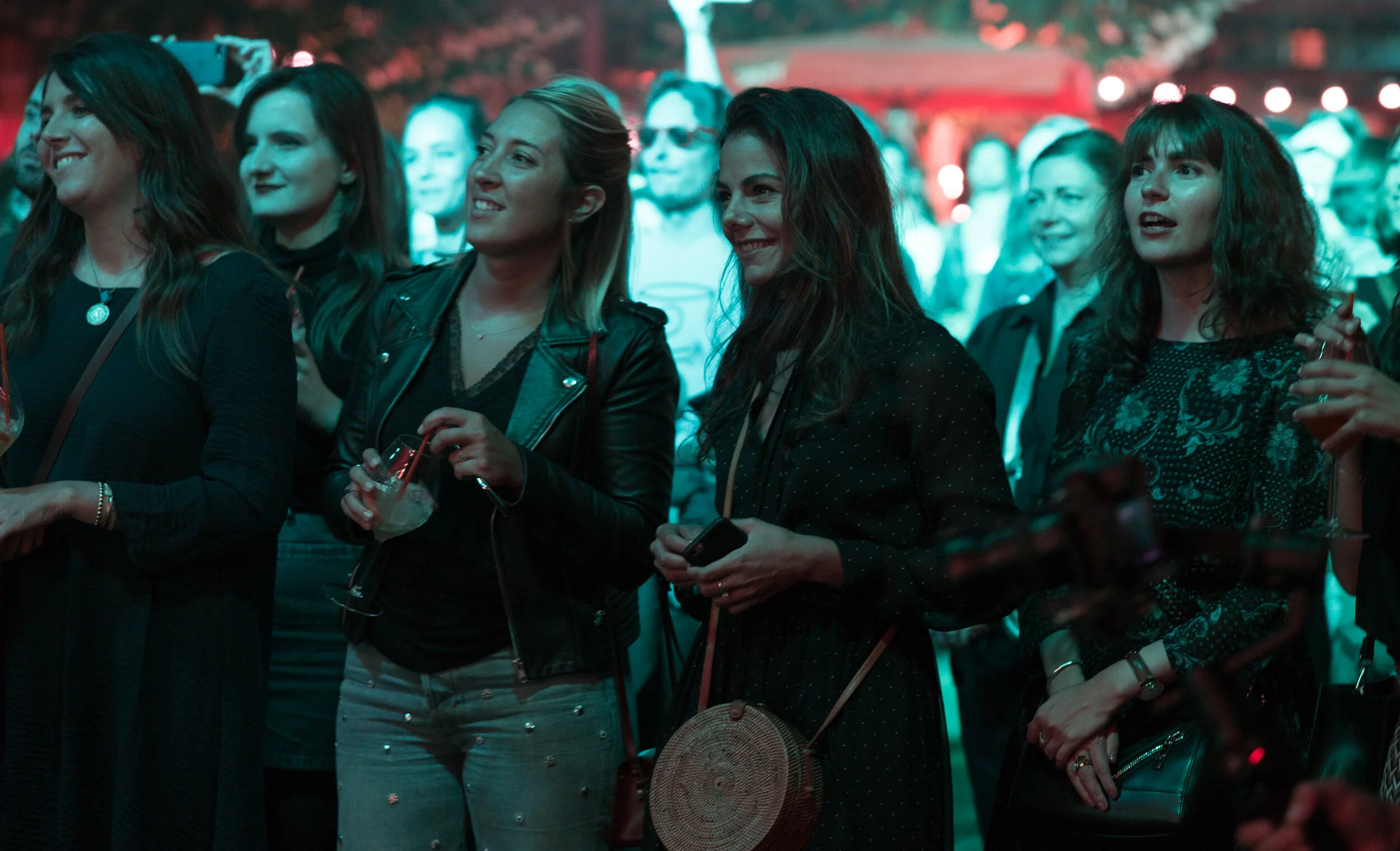 Groupe de jeunes femmes souriantes assistant à un événement en soirée avec éclairage coloré.