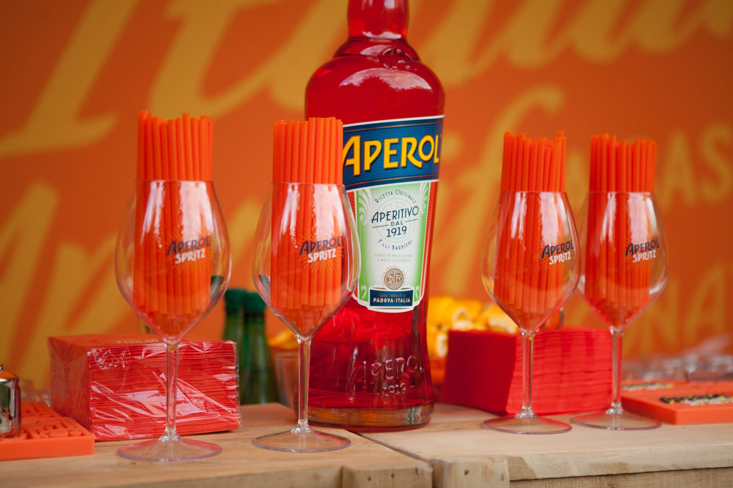 Verre à vin rempli de pailles orange avec bouteille d'Aperol en arrière-plan sur une table en bois